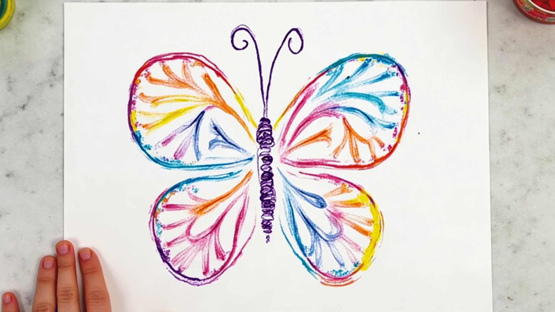 a bright watercolor butterfly on white paper with white crayon resist patterns showing through the wings