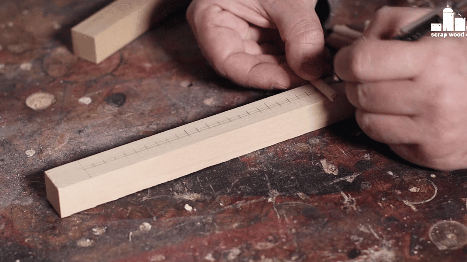 a person using a square tool to mark evenly spaced positions on a wooden piece for reed slots or pegs on a loom.
