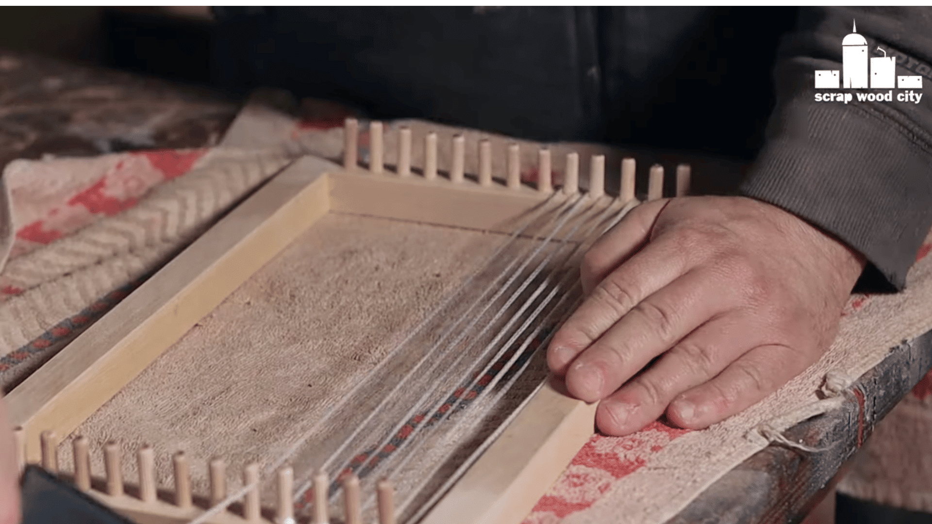 a person warping the loom by stretching yarn across the wooden pegs.