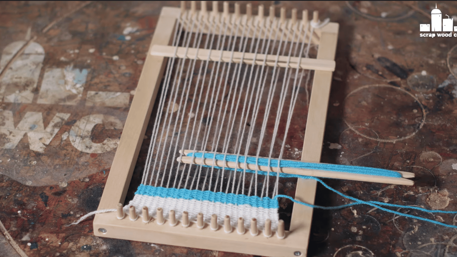 a person weaving yarn through the warp threads on a wooden loom using a shuttle.