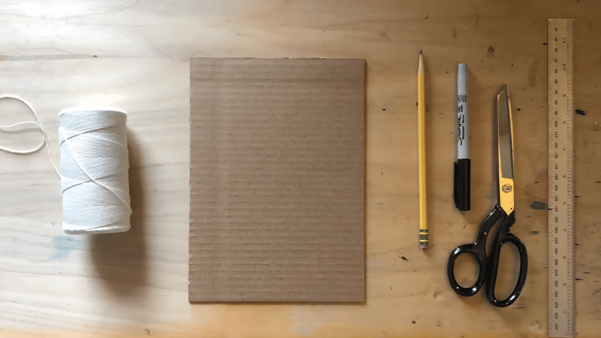 a ruler, marker, and a roll of thread next to a piece of cardboard as the first step to prepare for making a loom.