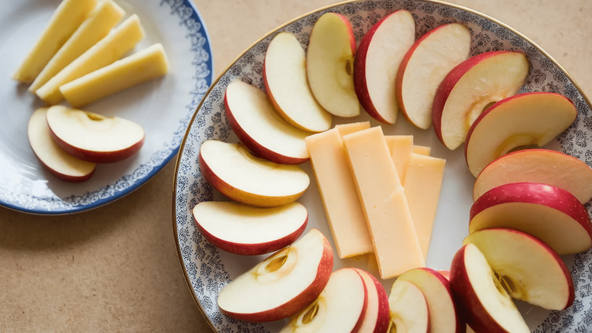 apple slices arranged in circle around cheese sticks on decorative plate with extra apple slices and cheese wedges on small plate nearby