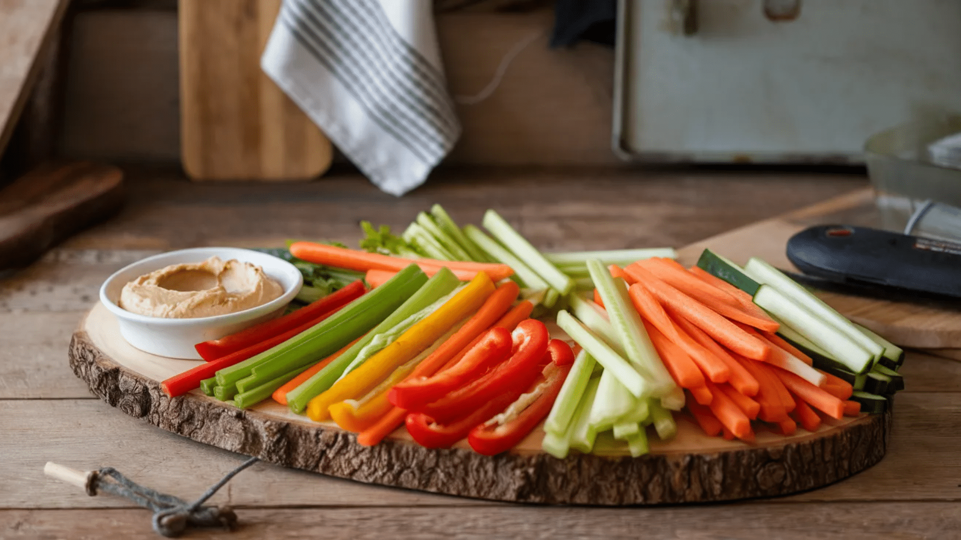 assorted fresh vegetable sticks including carrots celery cucumber and bell peppers arranged on wooden board with bowl of hummus dip