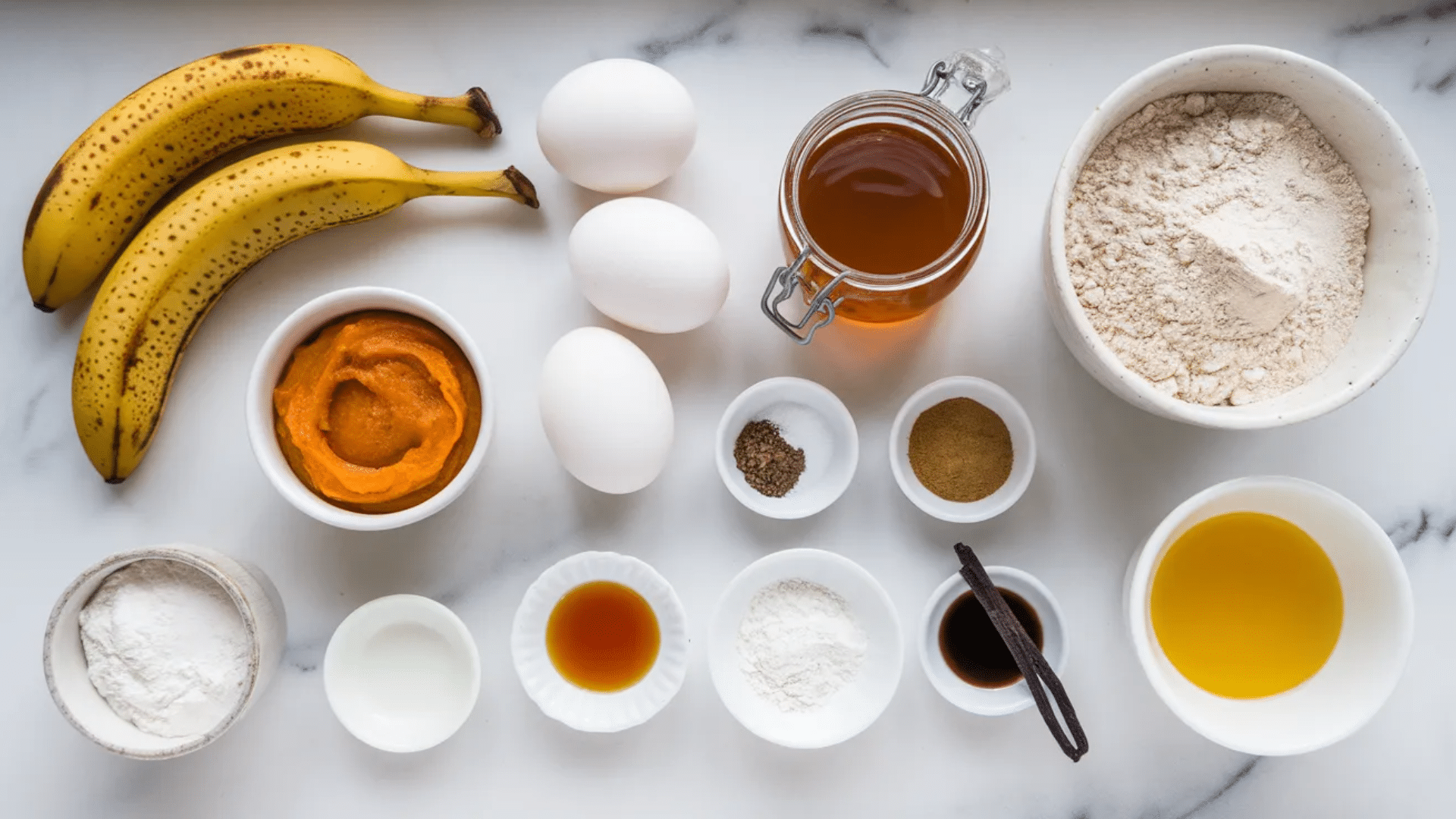 banana pumpkin muffin ingredients flat laid on a marble surface including ripe bananas, pumpkin puree, eggs, flour, maple syrup, and warm spices