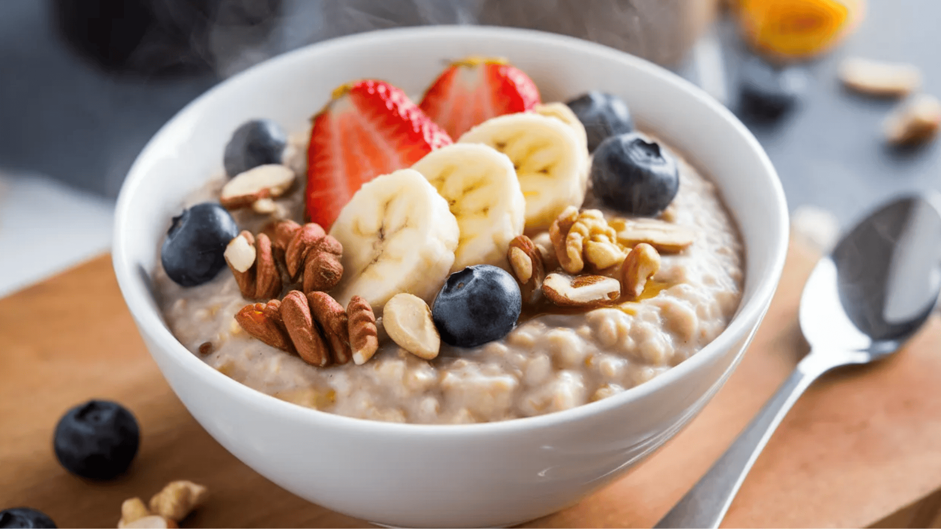 bowl of oatmeal topped with sliced banana, strawberries, blueberries, and mixed nuts