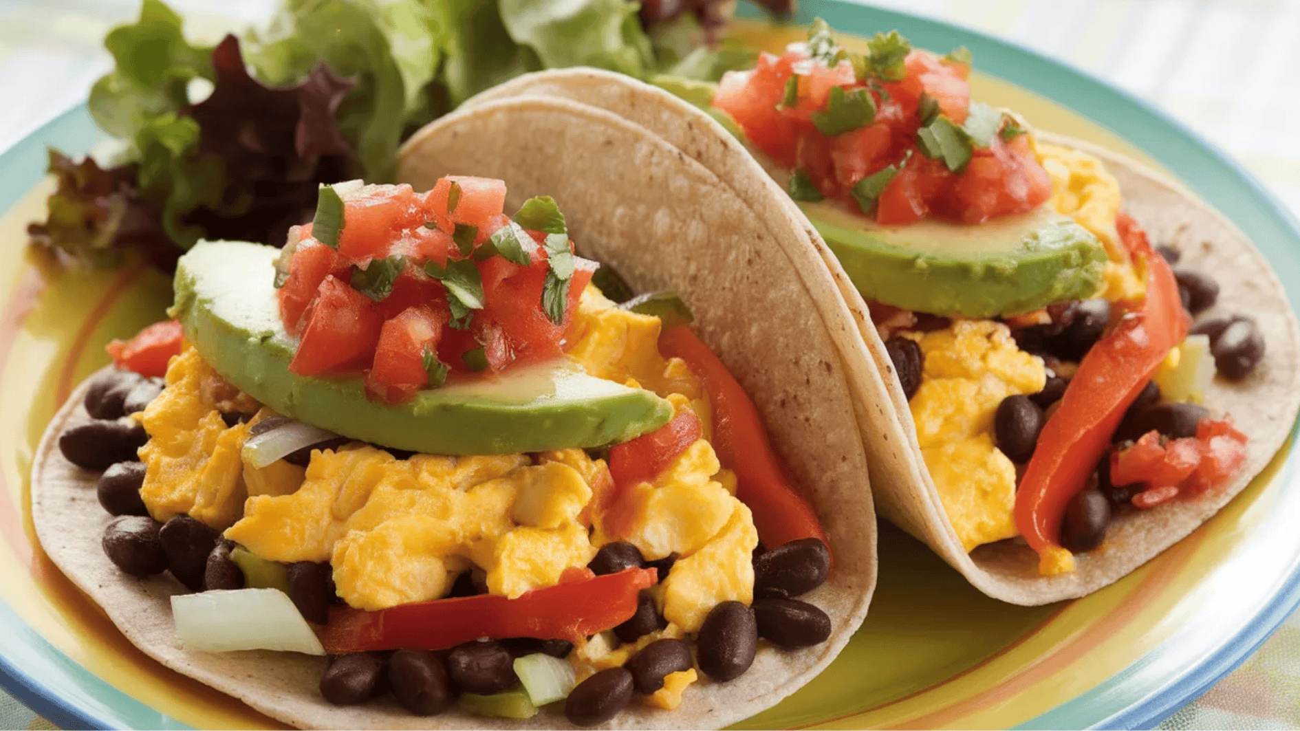 breakfast tacos filled with scrambled eggs, black beans, avocado, tomatoes, and red peppers, garnished with cilantro