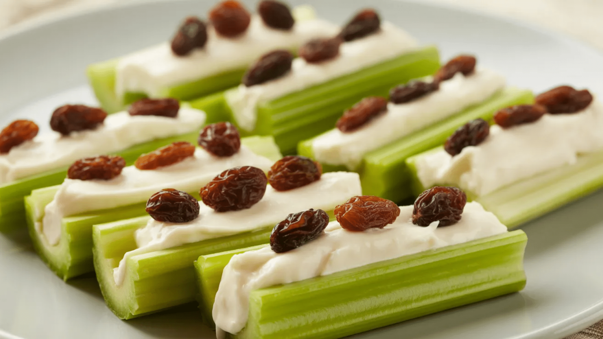 celery sticks filled with creamy spread and topped with raisins arranged on plate forming classic ants on a log snack presentation (1)