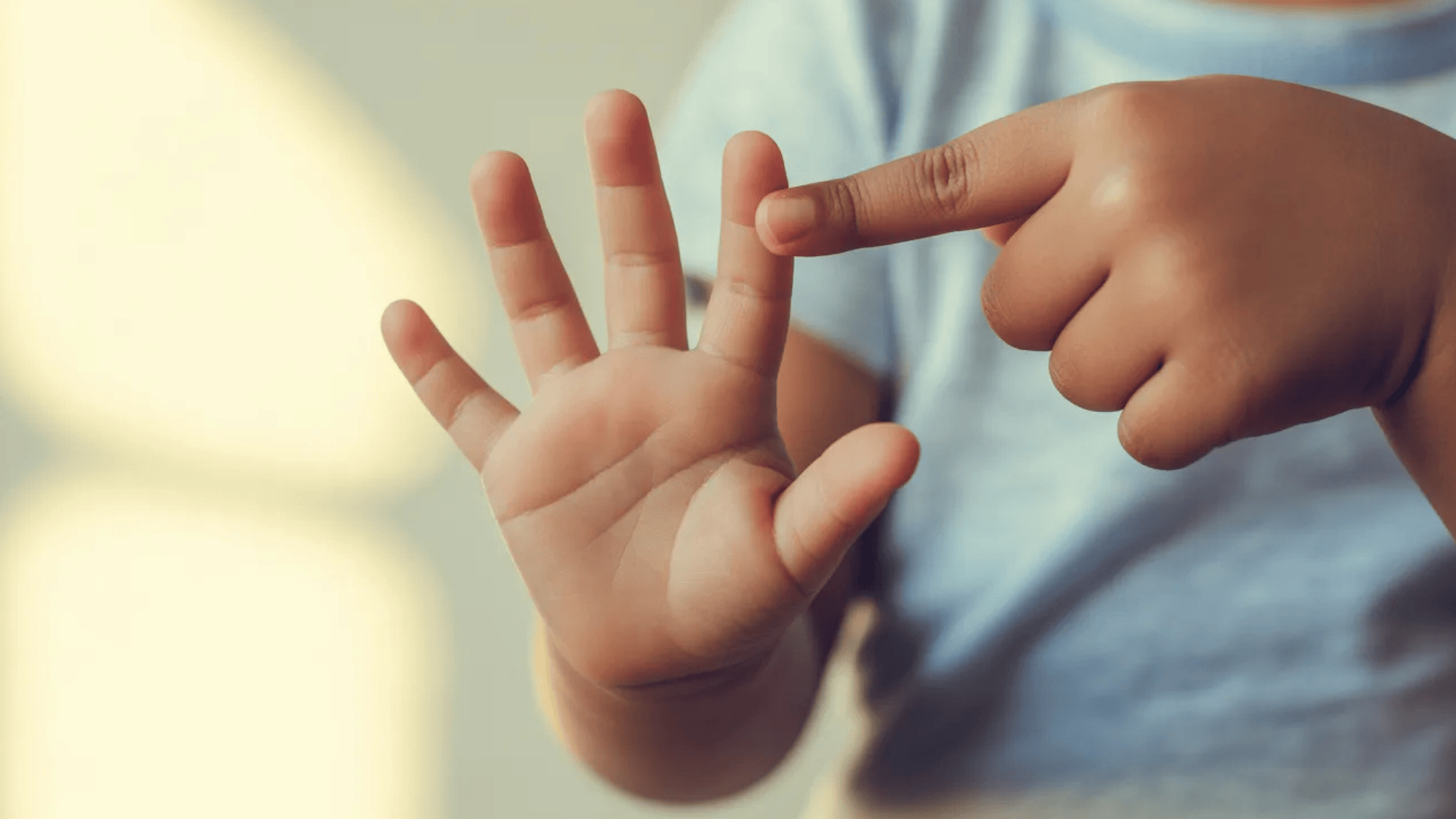close-up of a child pointing at their hand, showing the fingers