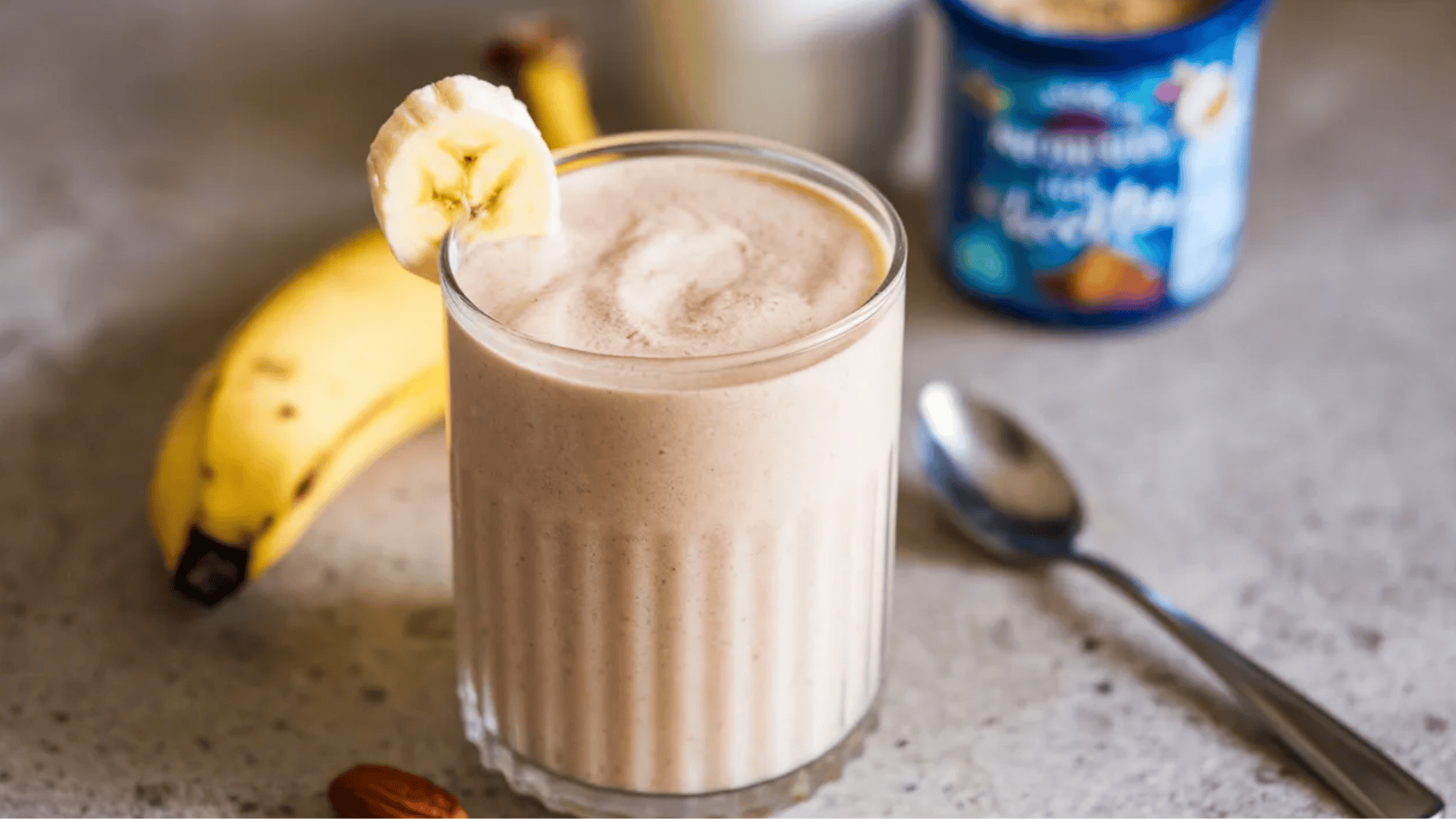 creamy banana smoothie topped with a banana slice, with a spoon and a banana in the background