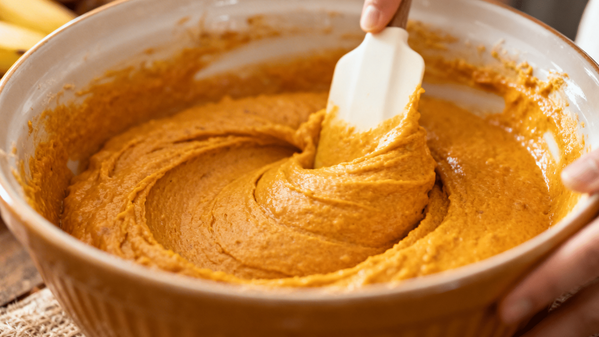 folding thick pumpkin banana muffin batter gently with a spatula in a mixing bowl.