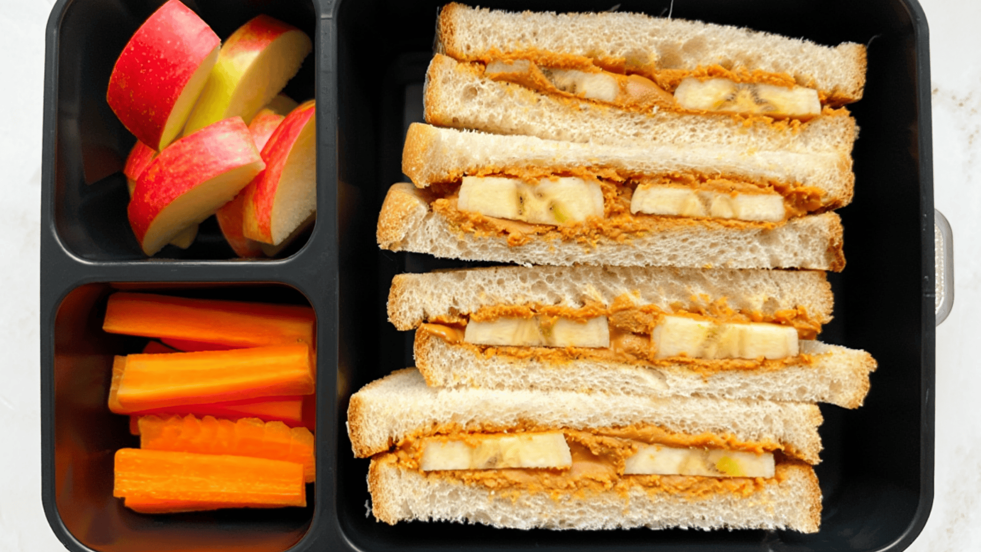 four peanut butter and banana Sandwiches with fruits in a lunchbox