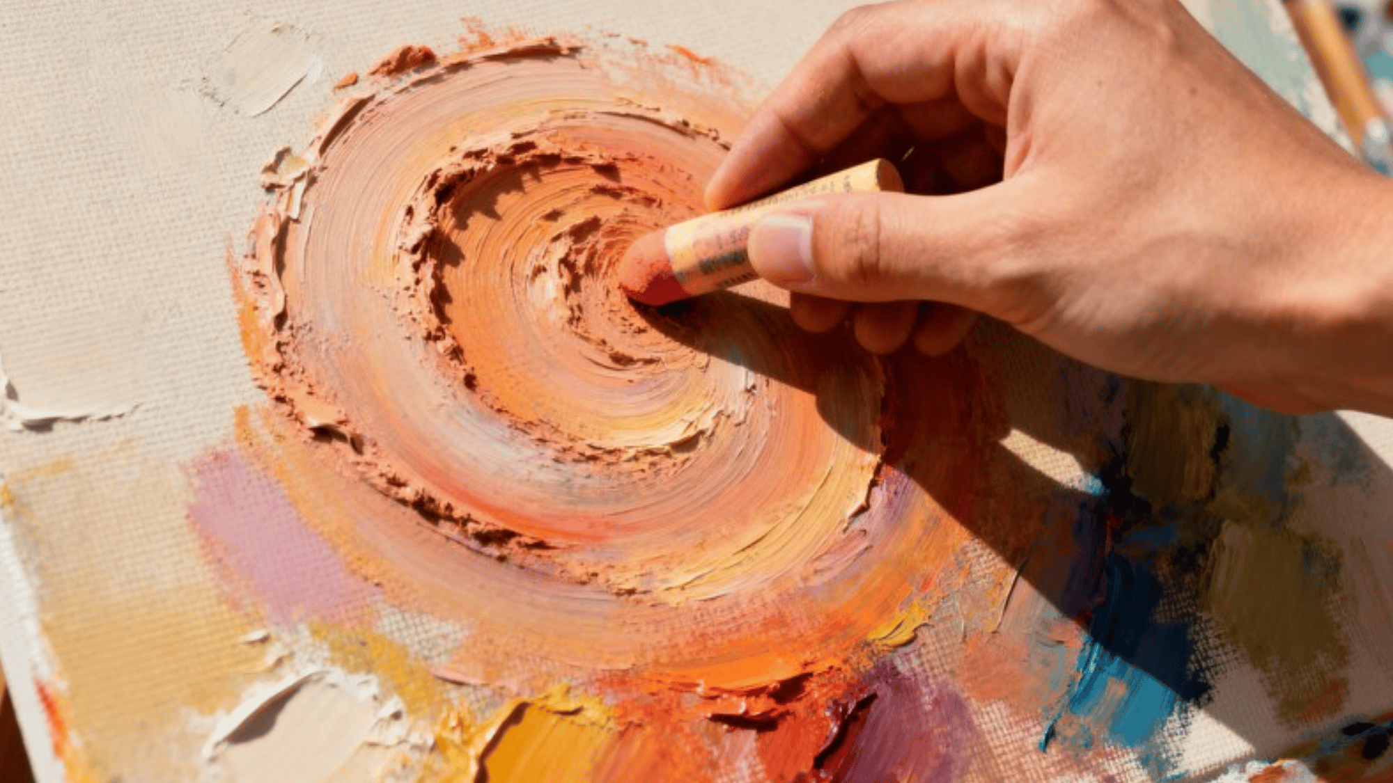 hand using a pastel stick to create a swirling scumbling effect on a textured canvas with warm, vibrant colors