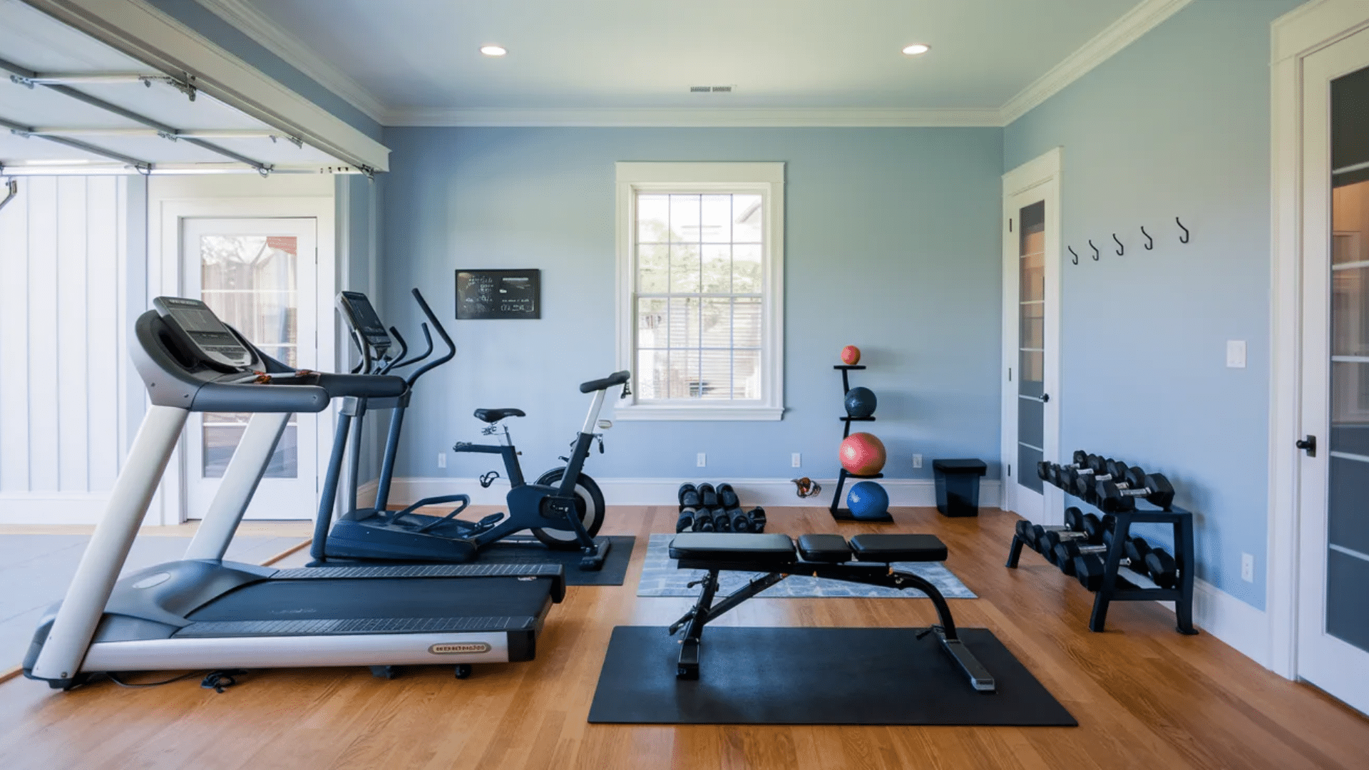 home gym with treadmill exercise bike weight bench dumbbells rack yoga mats and colorful exercise balls on wooden floor