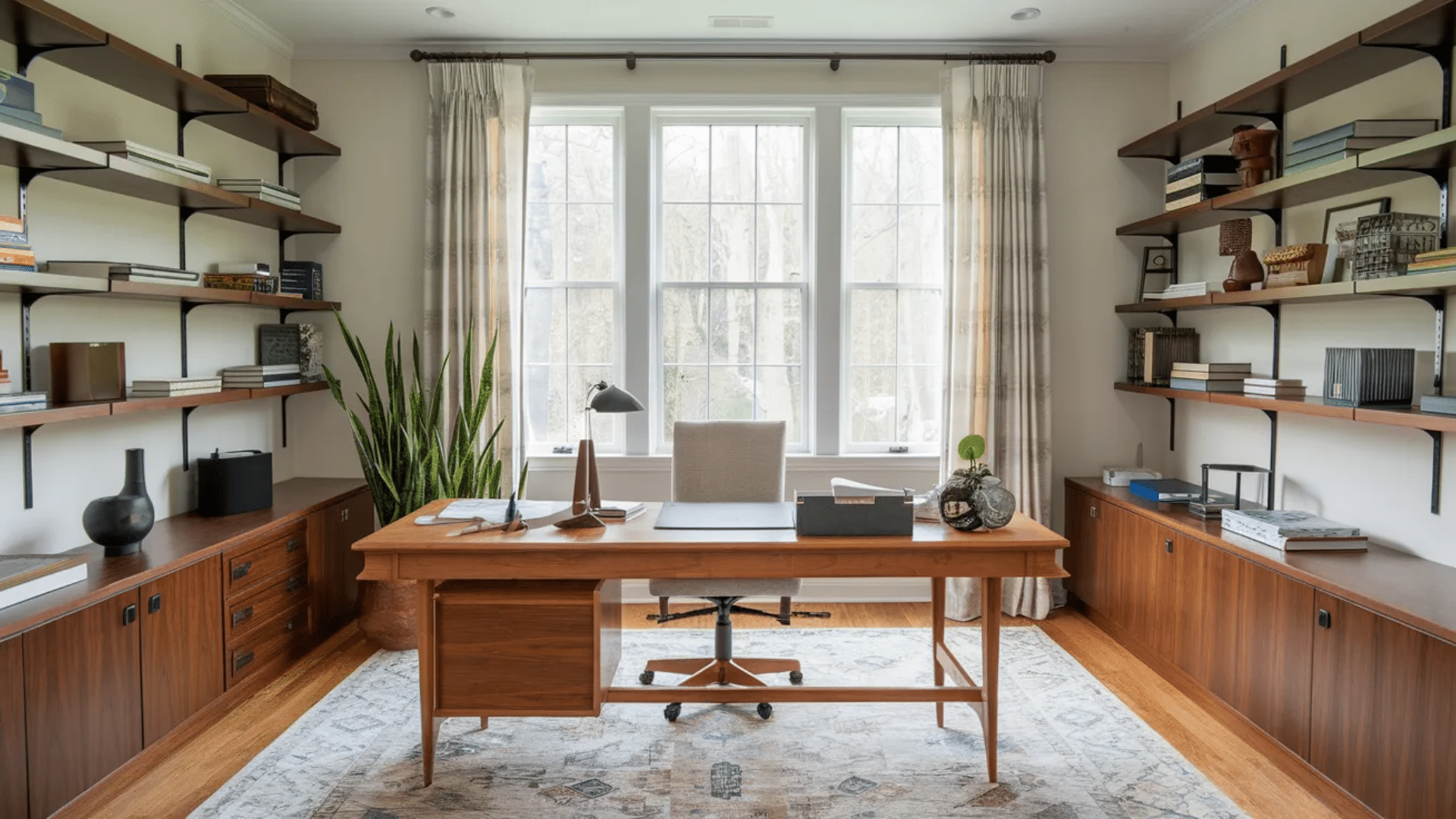 home office with wooden desk large window floating shelves with books cabinets plants and neutral rug in bright workspace