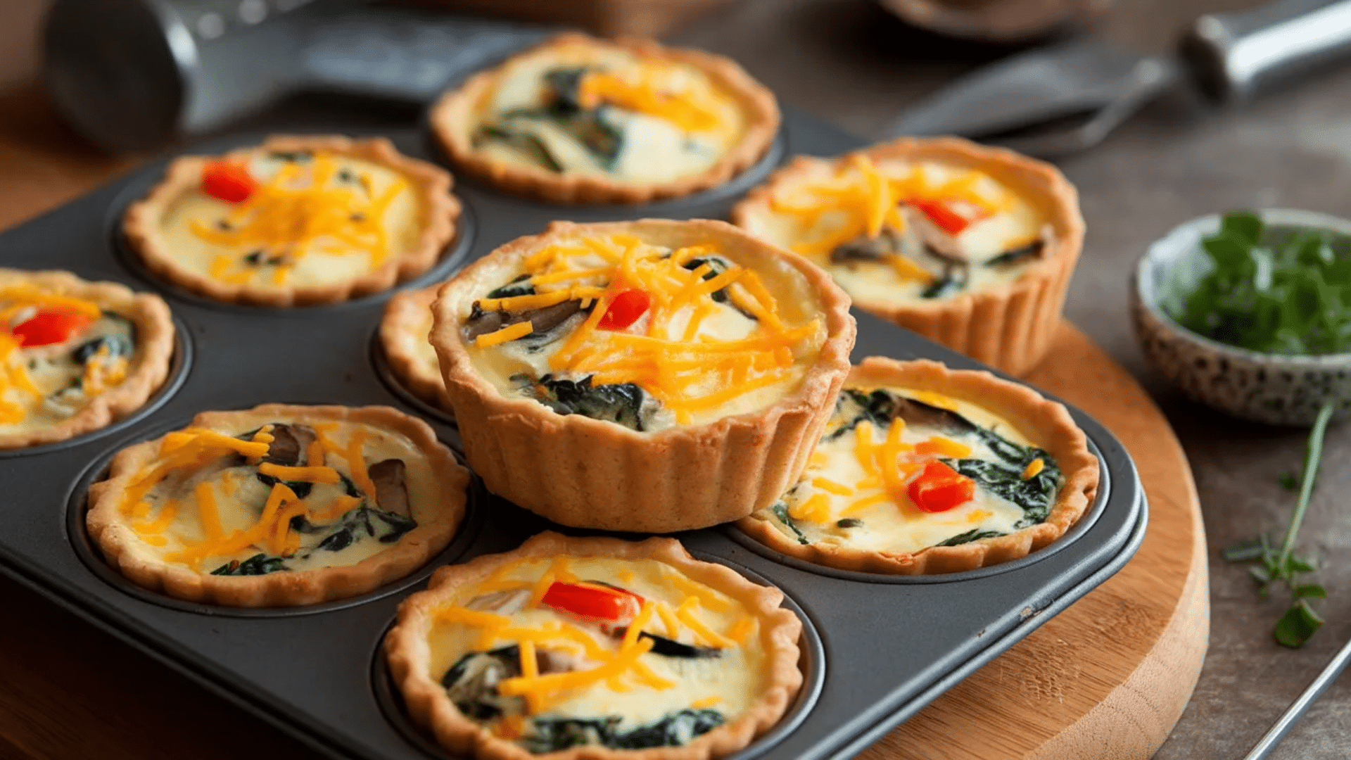 mini quiches with spinach mushrooms and cheese baked in muffin tin with one quiche stacked on top on wooden board