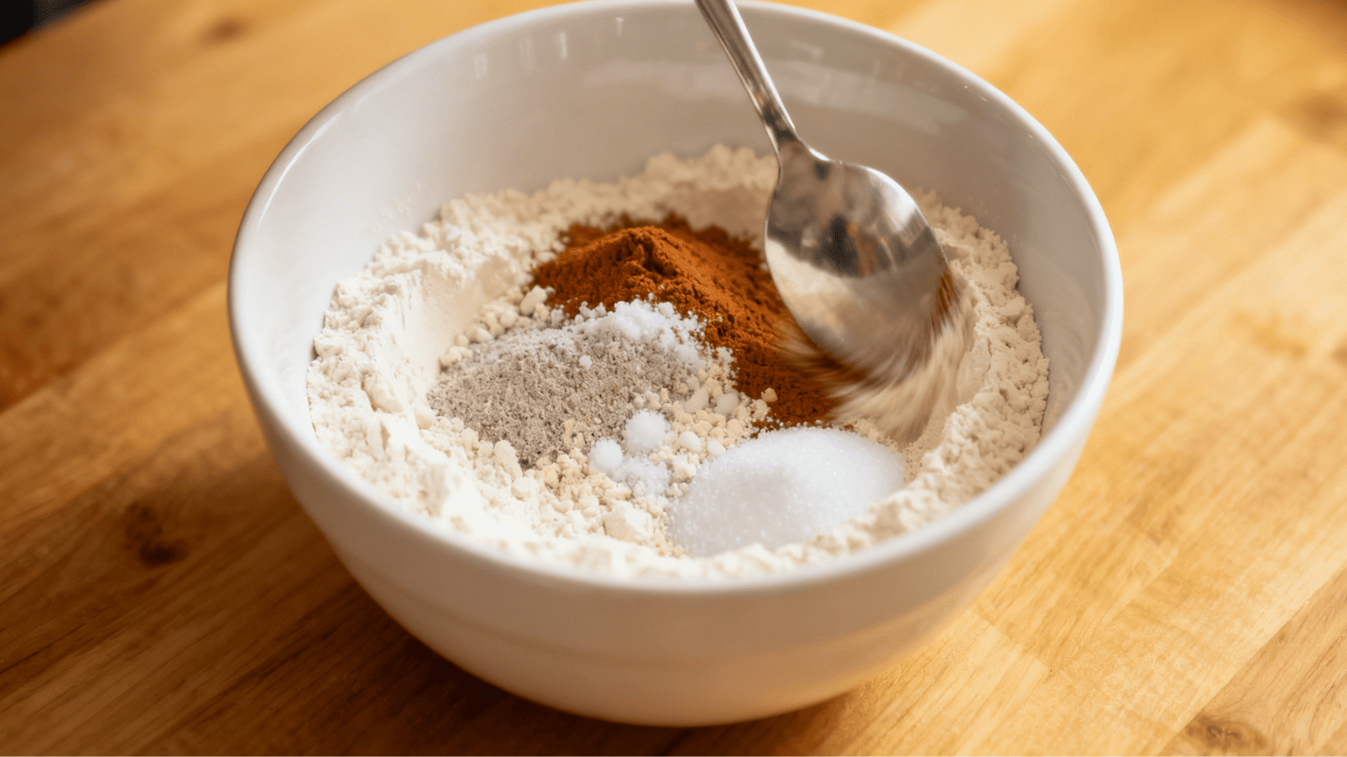 mixing dry baking ingredients like flour cinnamon sugar and baking powder in a bowl with a spoon