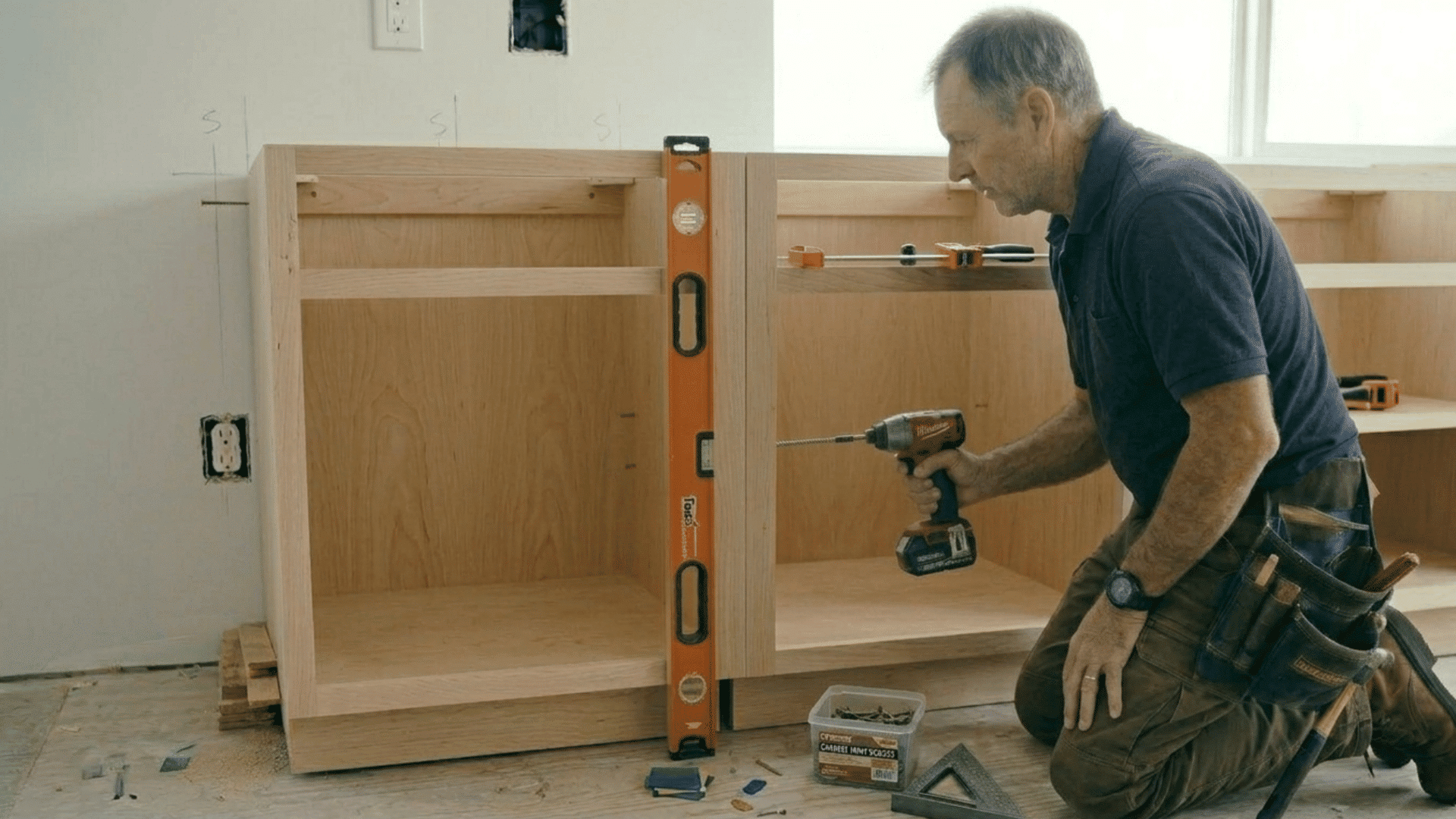 moving a complete cabinet unit into place, checking alignment, and securing it to the wall studs for final installation