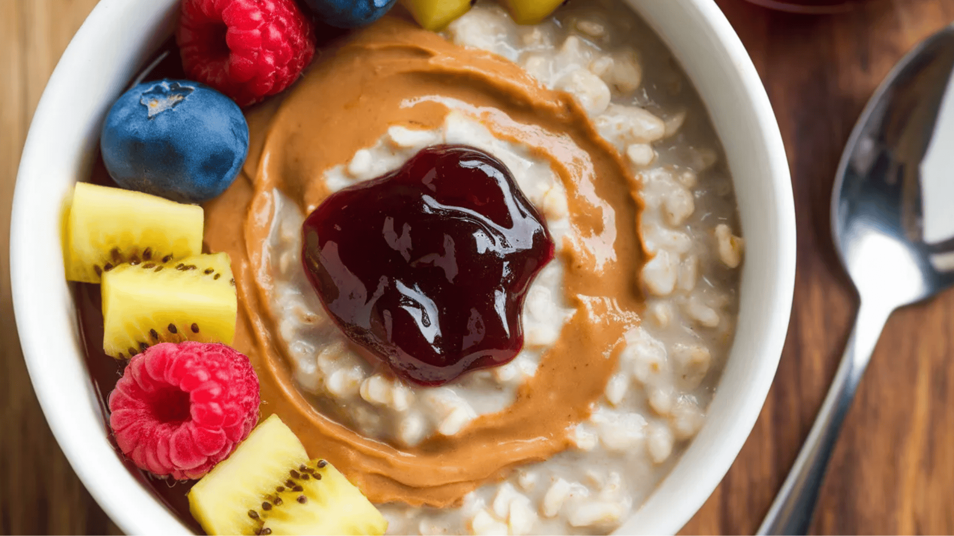 oatmeal topped with almond butter, jelly, and fresh fruits like raspberries, blueberries, and kiwi slices