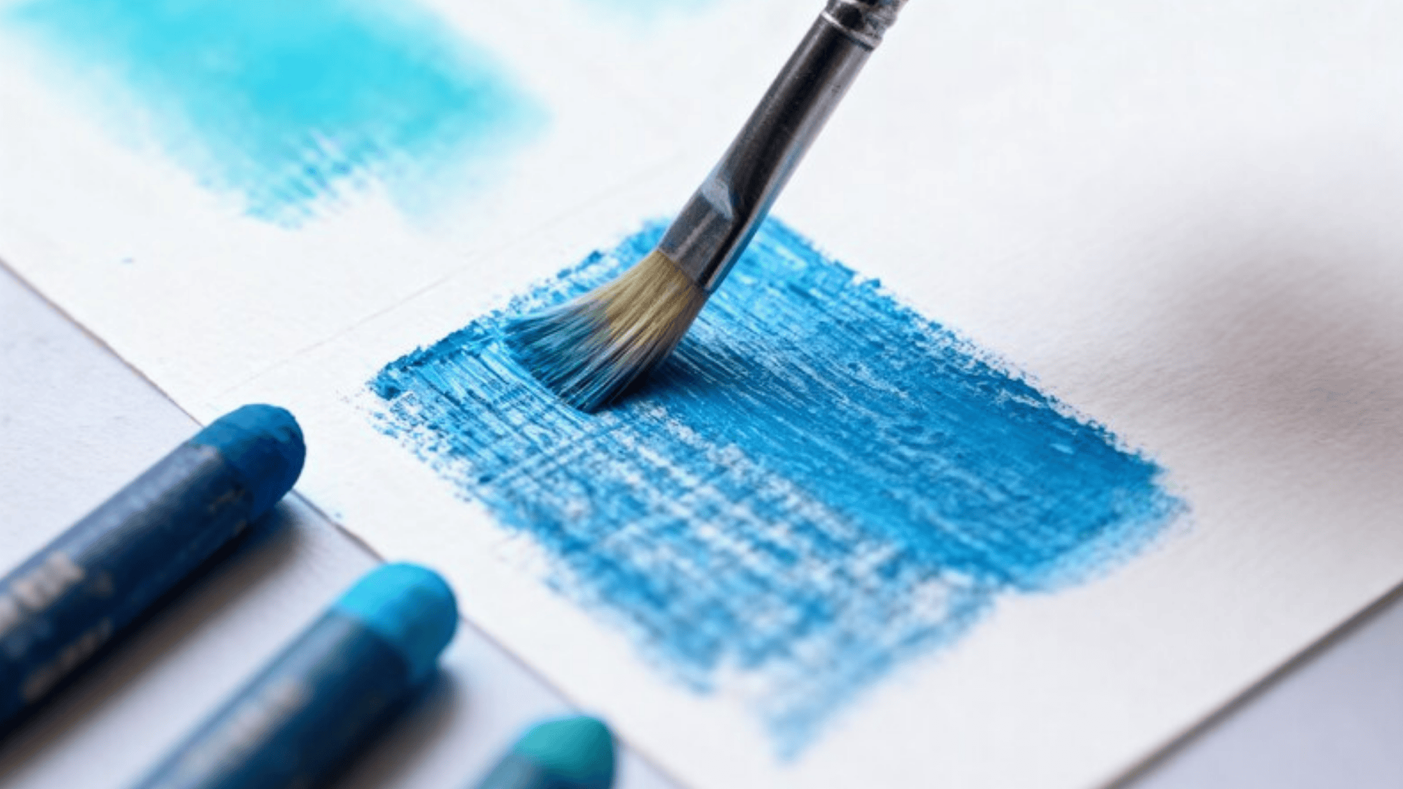 paintbrush blending blue pastel on textured paper, with a few blue pastels resting nearby