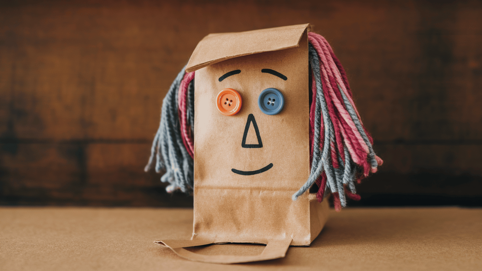paper bag puppet with face drawn, yarn glued for hair, button eyes, sitting on a flat surface