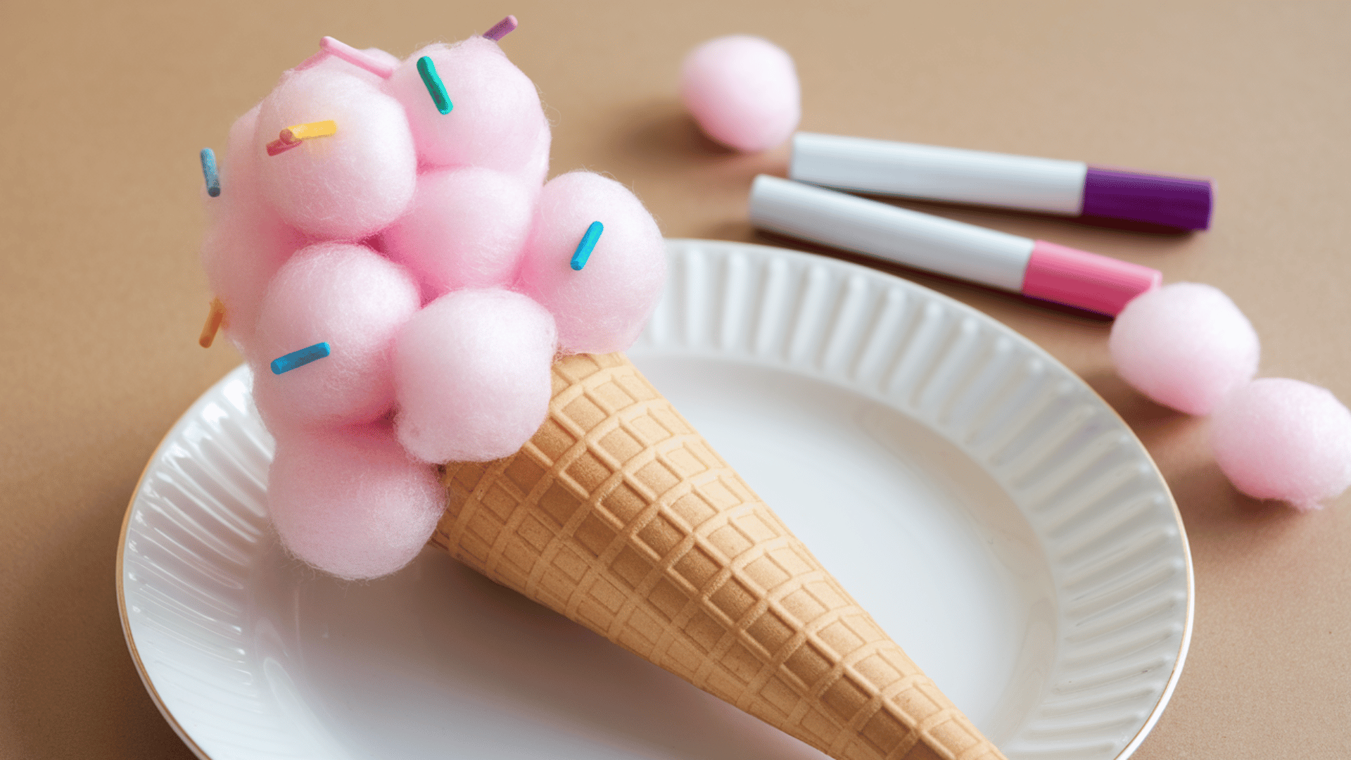 paper cone with pink cotton balls stacked as ice cream scoop, decorated with colorful sprinkles.