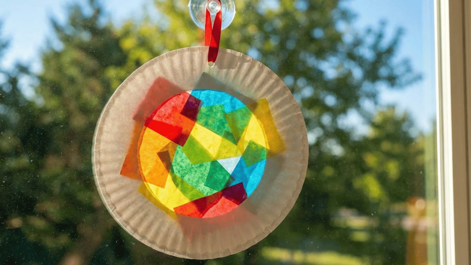 paper plate with center cut out, colorful tissue paper in stained-glass pattern, ribbon for hanging, placed against window.