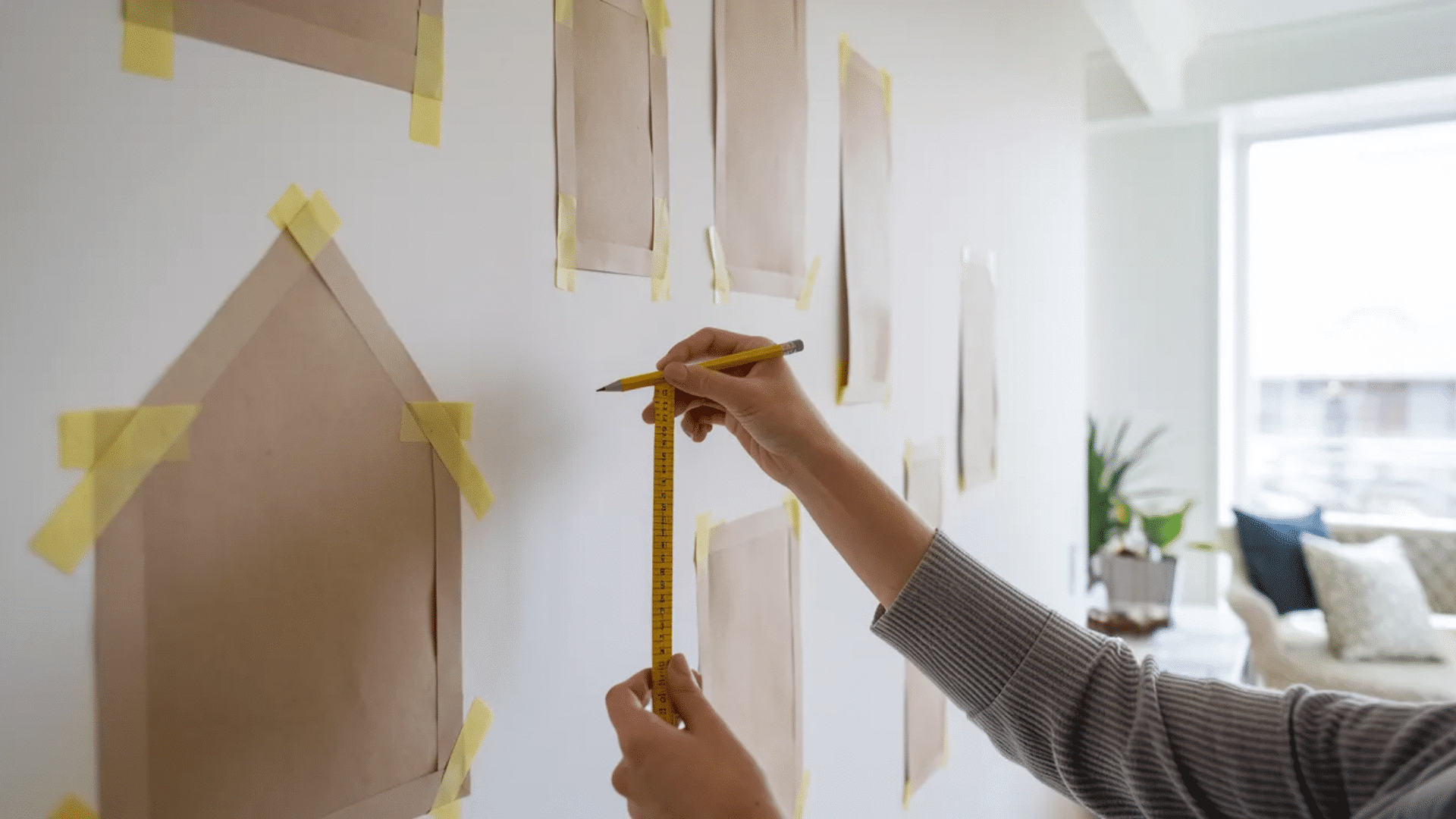 paper templates taped to a wall showing picture frame layout while a person adjusts spacing before hanging artwork