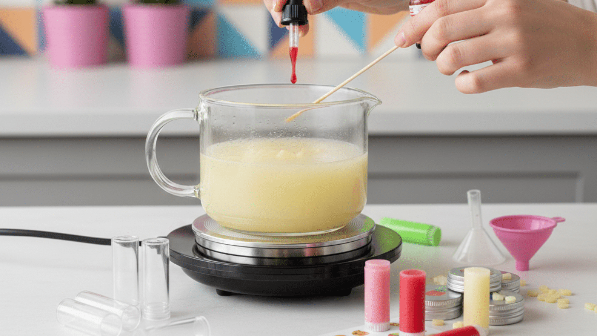 person adds red coloring to a melting wax mixture in a glass container while preparing DIY lip balm