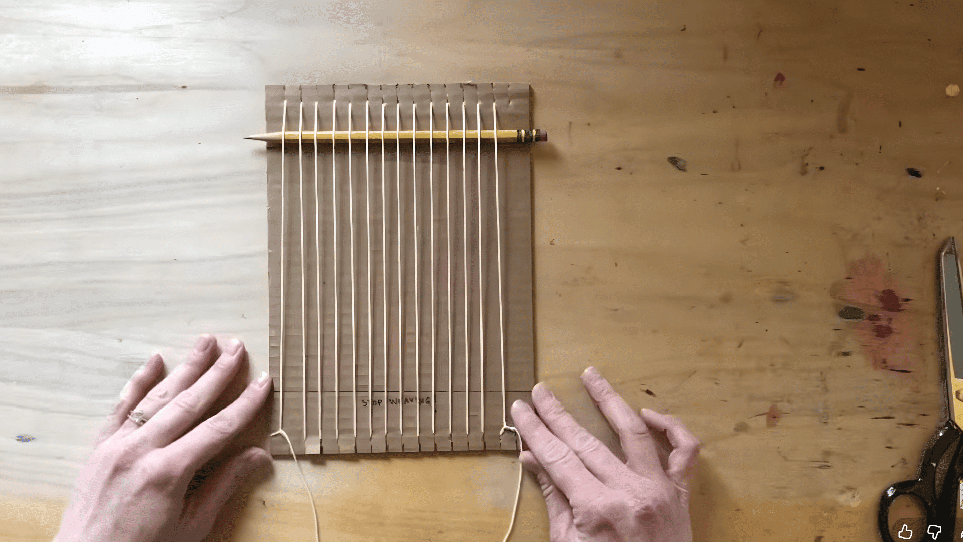 placing a pencil behind the warp threads on the cardboard loom to help with the weaving process