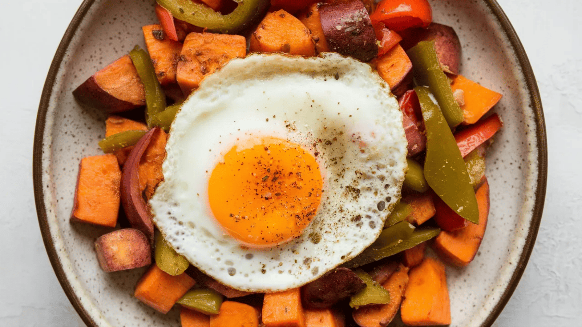 plate of roasted sweet potatoes, bell peppers, and jalapeños topped with a fried egg and seasoned with black pepper