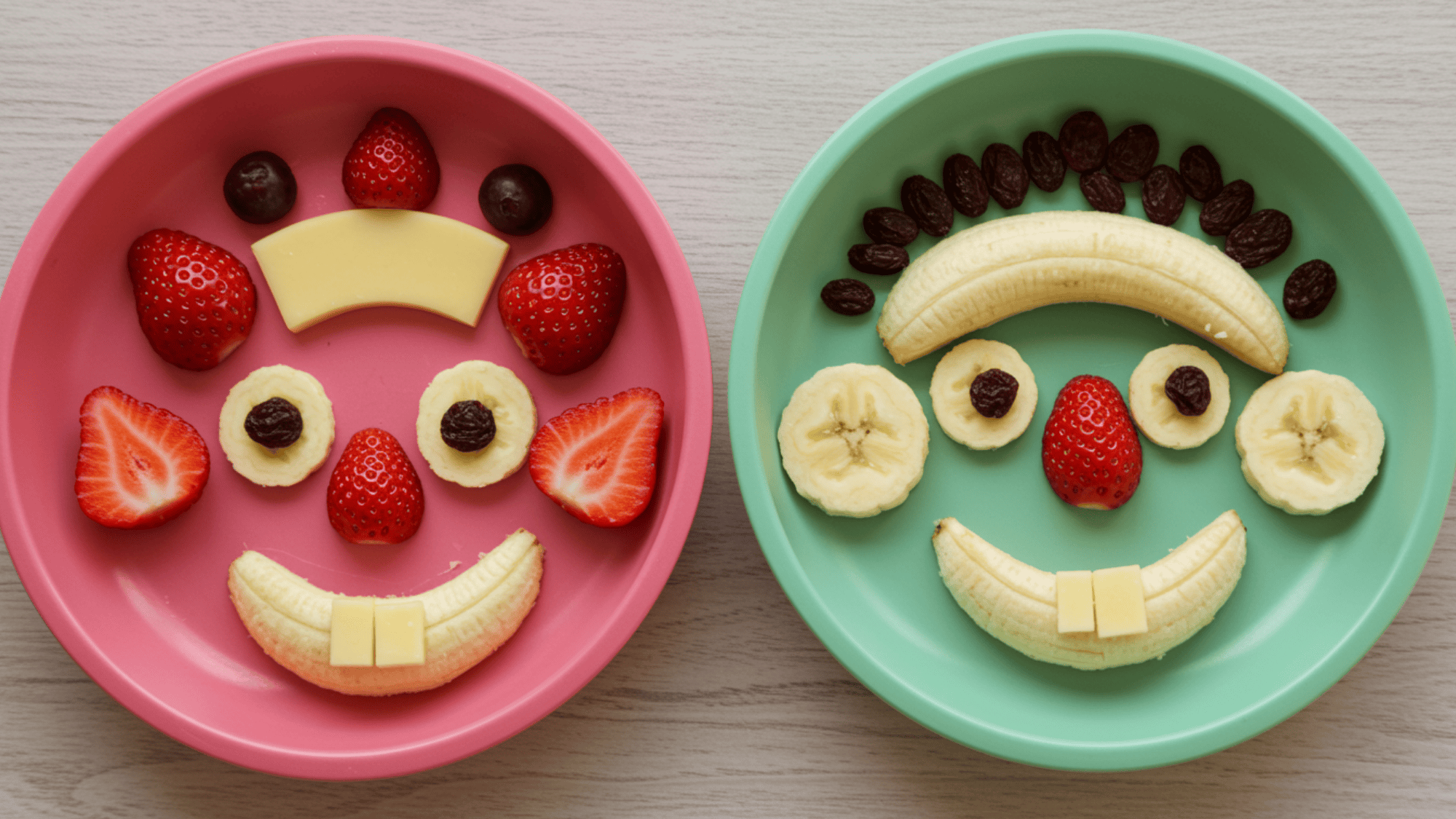 playful lunchbox plate with fruit faces made of banana smiles, strawberry cheeks, raisin eyes, cheese teeth