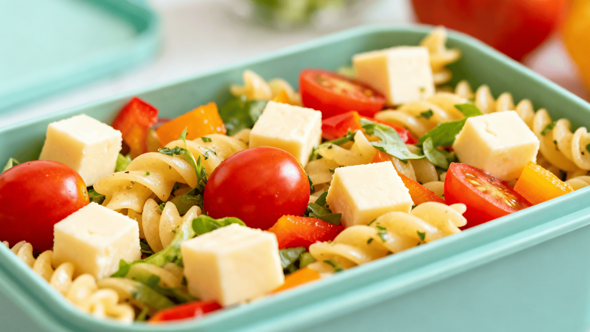 quick pasta salad with cheese cubes and colorful veggies in a lunchbox, vibrant cherry tomatoes and bell peppers
