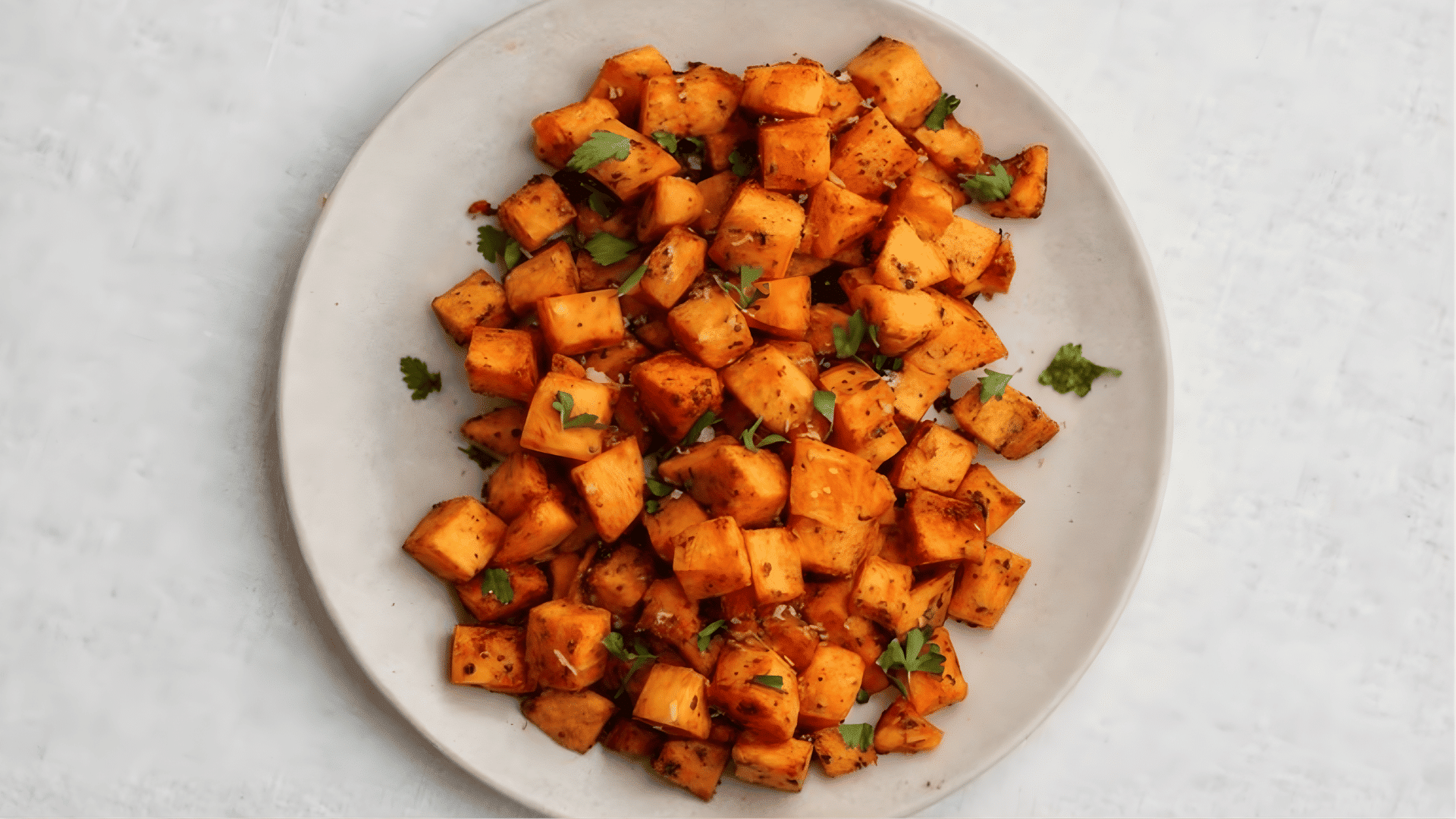roasted sweet potato cubes seasoned with spices and herbs served on a beige plate, viewed from above on a light background (1)