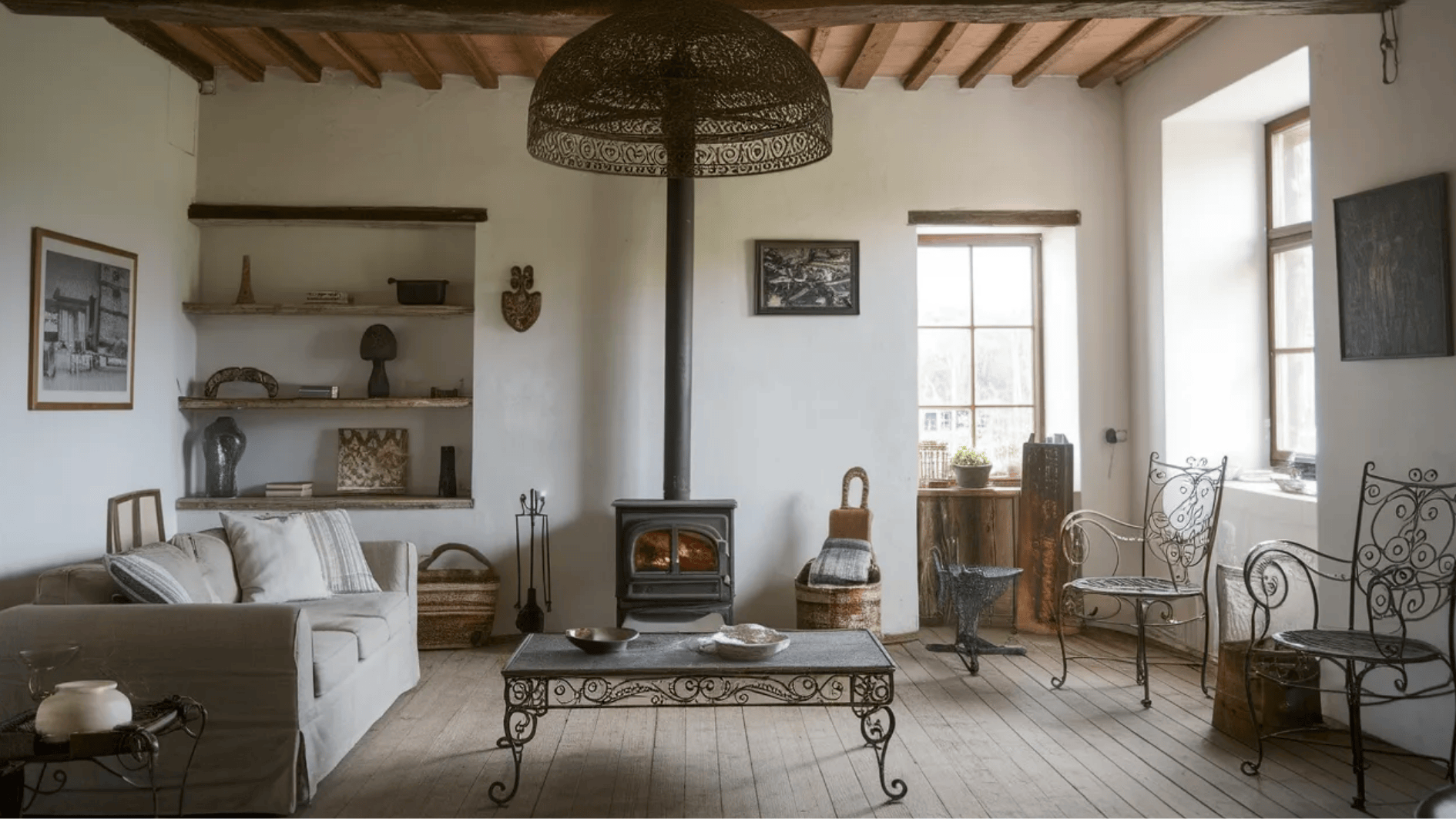 rustic living room featuring a cozy sofa, vintage metal chairs, and a wood stove, with simple shelves displaying decor