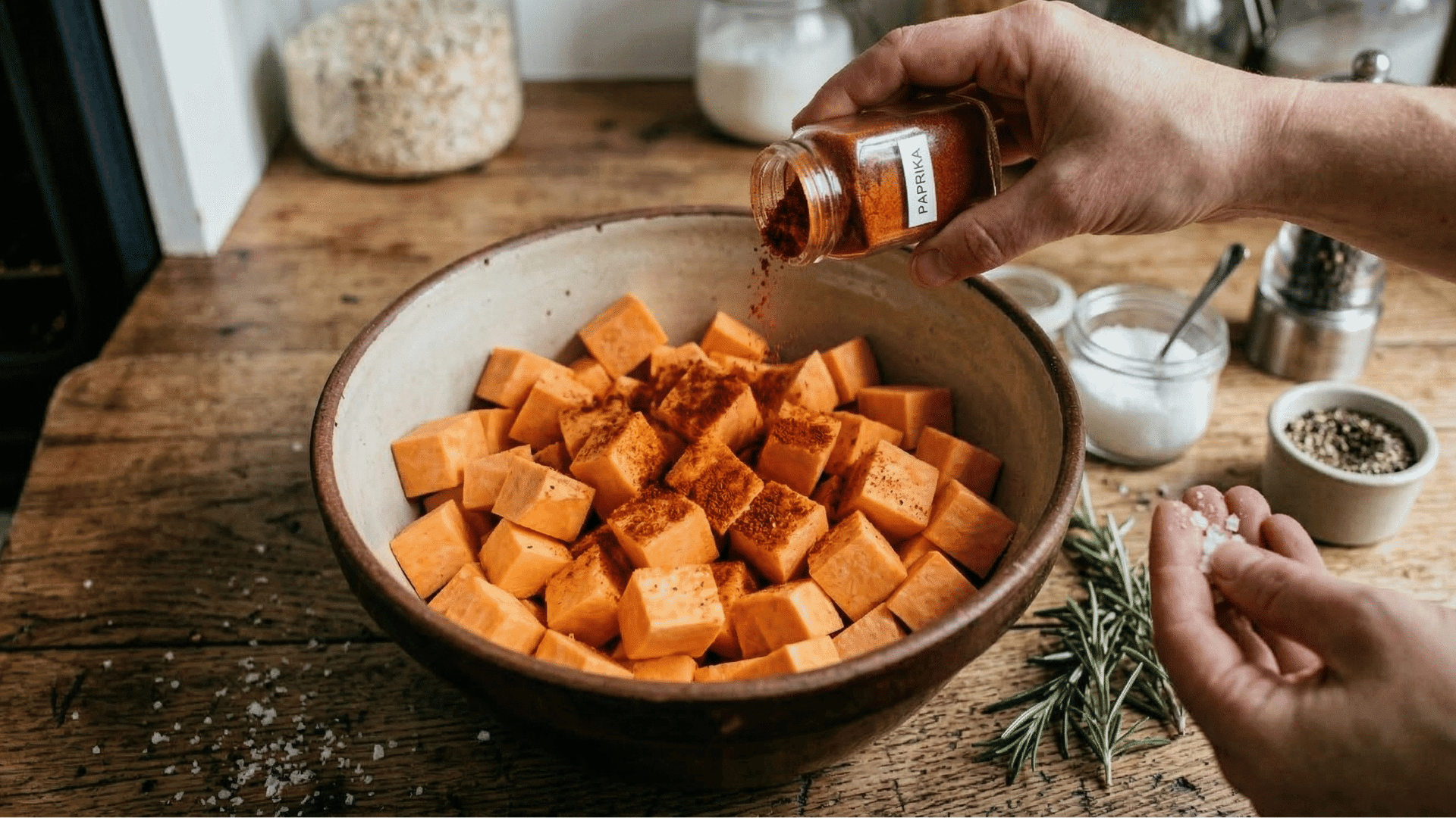 seasoned sweet potato cubes with spices like paprika, salt and pepper mixing in the bowl.