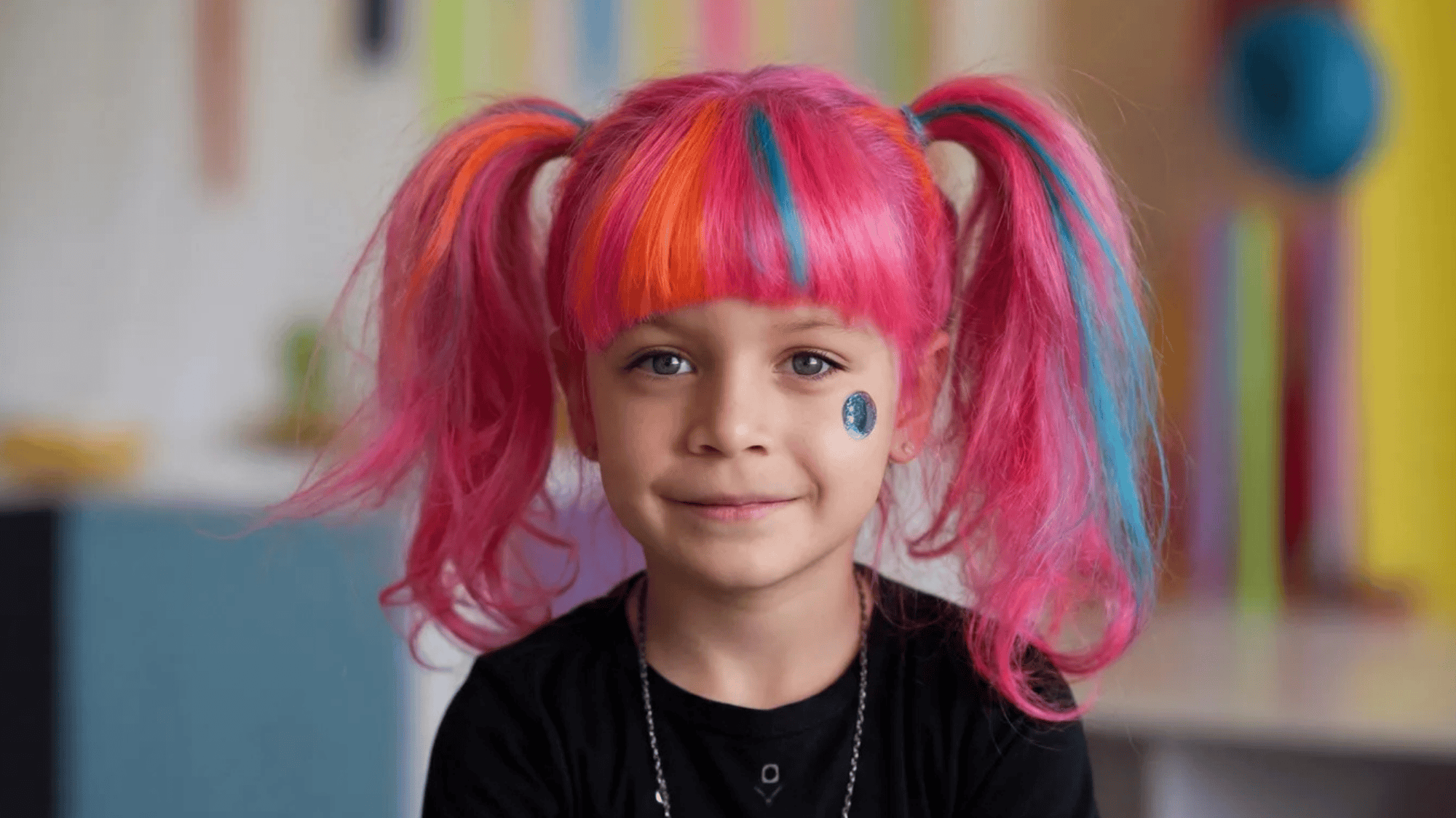 smiling girl with vibrant pink, orange, and blue hair pigtails, featuring a shiny sticker on her cheek, against a colorful background