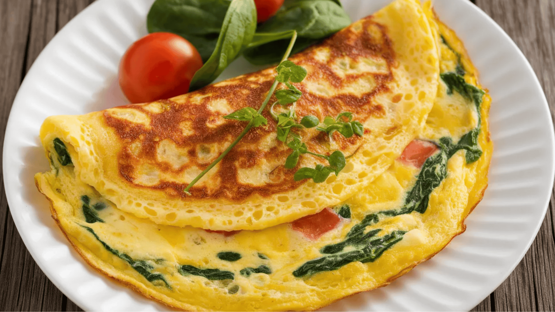 spinach and tomato omelette garnished with fresh herbs, served with a side of spinach and cherry tomatoes