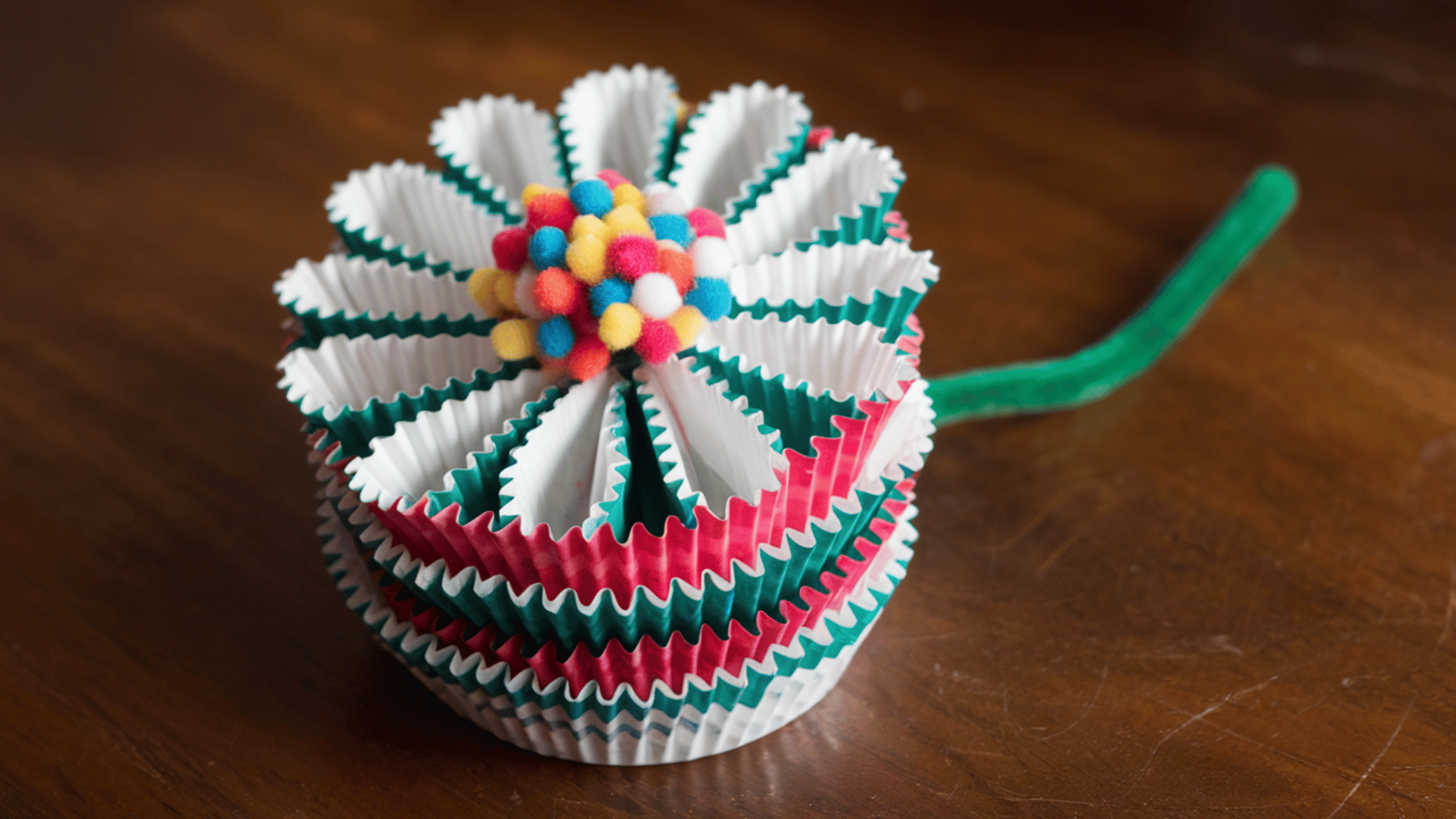 stacked cupcake liners glued together to form a flower, pom-pom center, green pipe cleaner stem