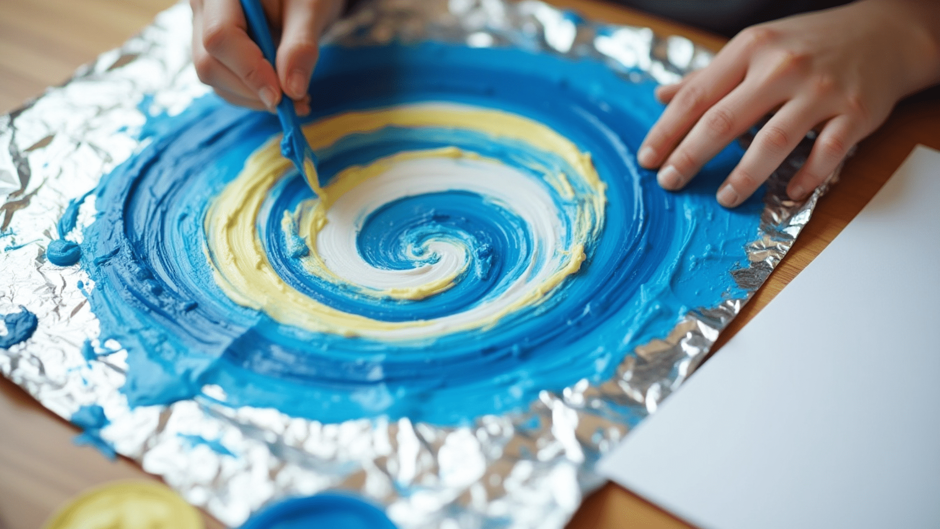 swirling blue and yellow finger paint marks blended across shiny aluminum foil