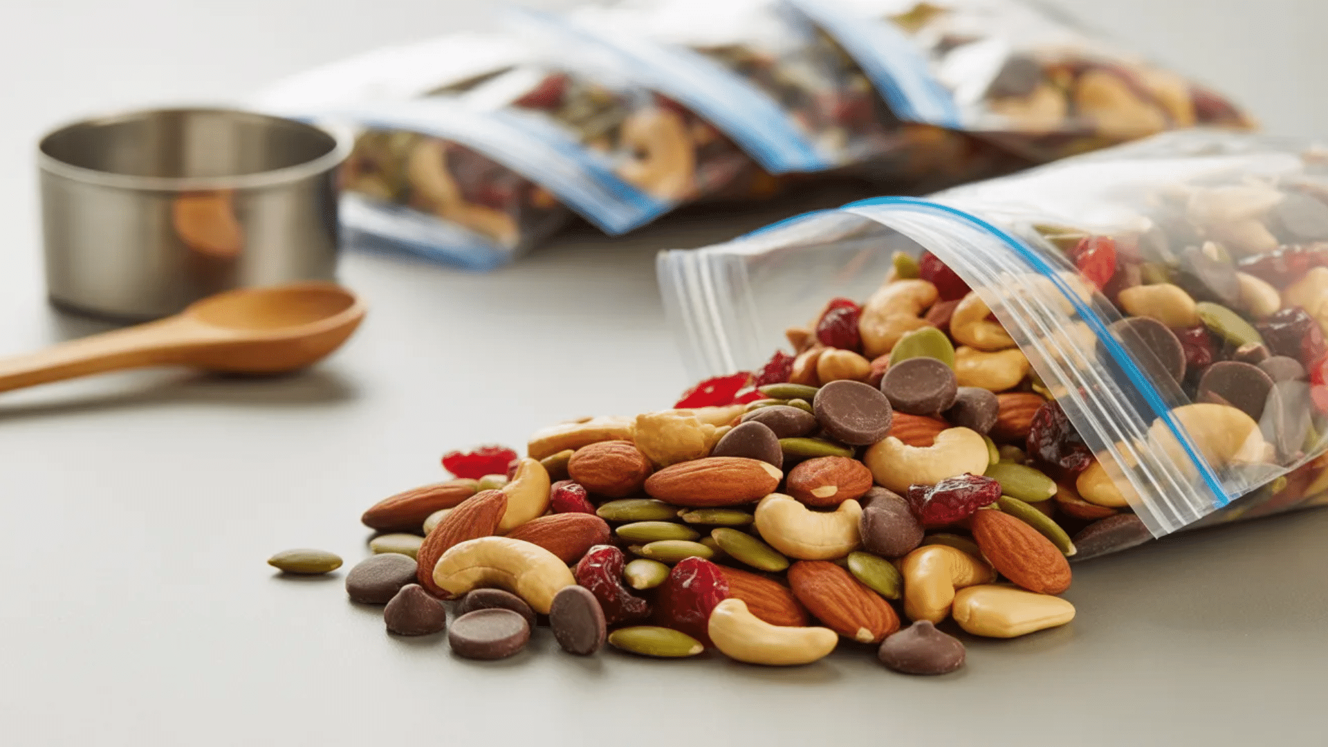 trail mix with almonds cashews pumpkin seeds dried cranberries and chocolate chips spilling from small resealable snack bags on table