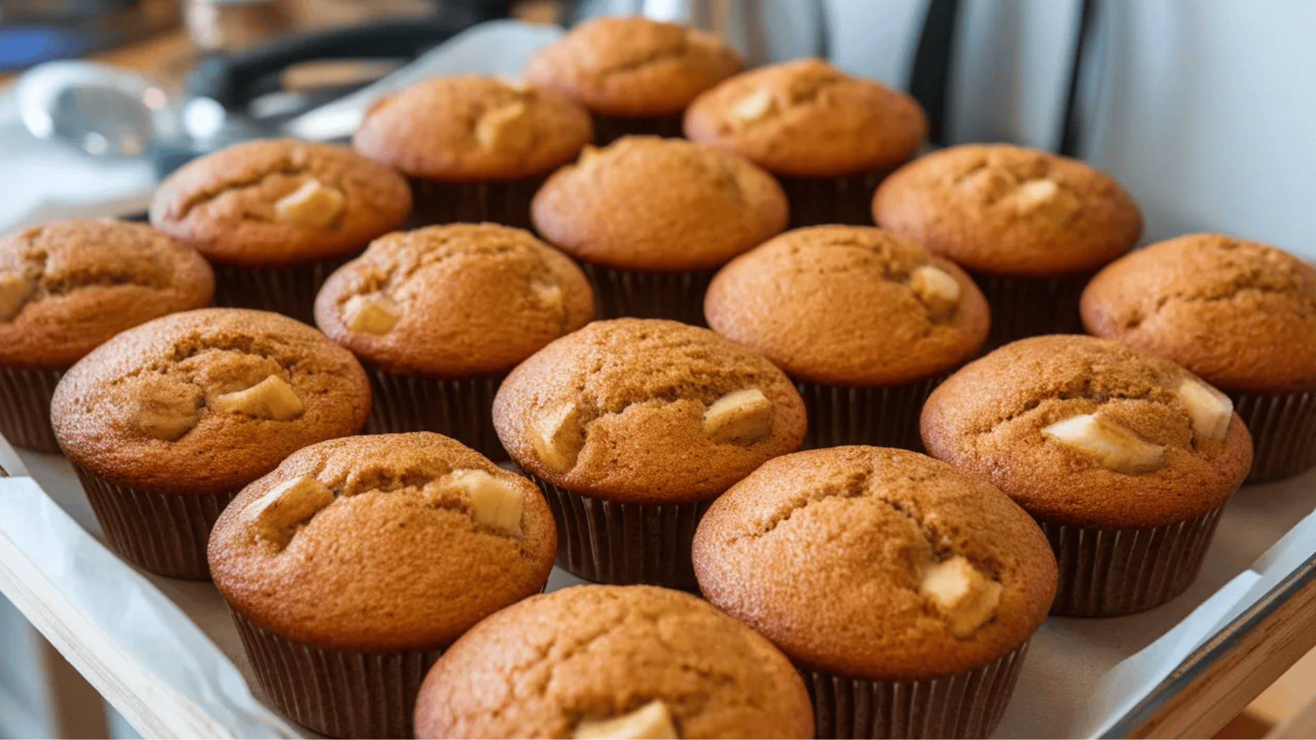 tray of freshly baked banana muffins with chunks of banana inside, neatly arranged in brown paper liners