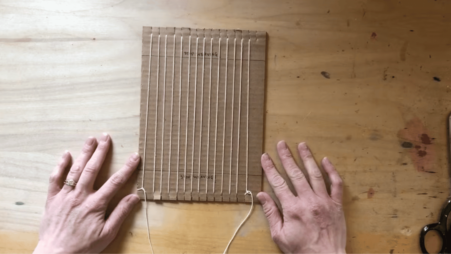 tying off the warp thread at the bottom of the loom, completing the warp setup.