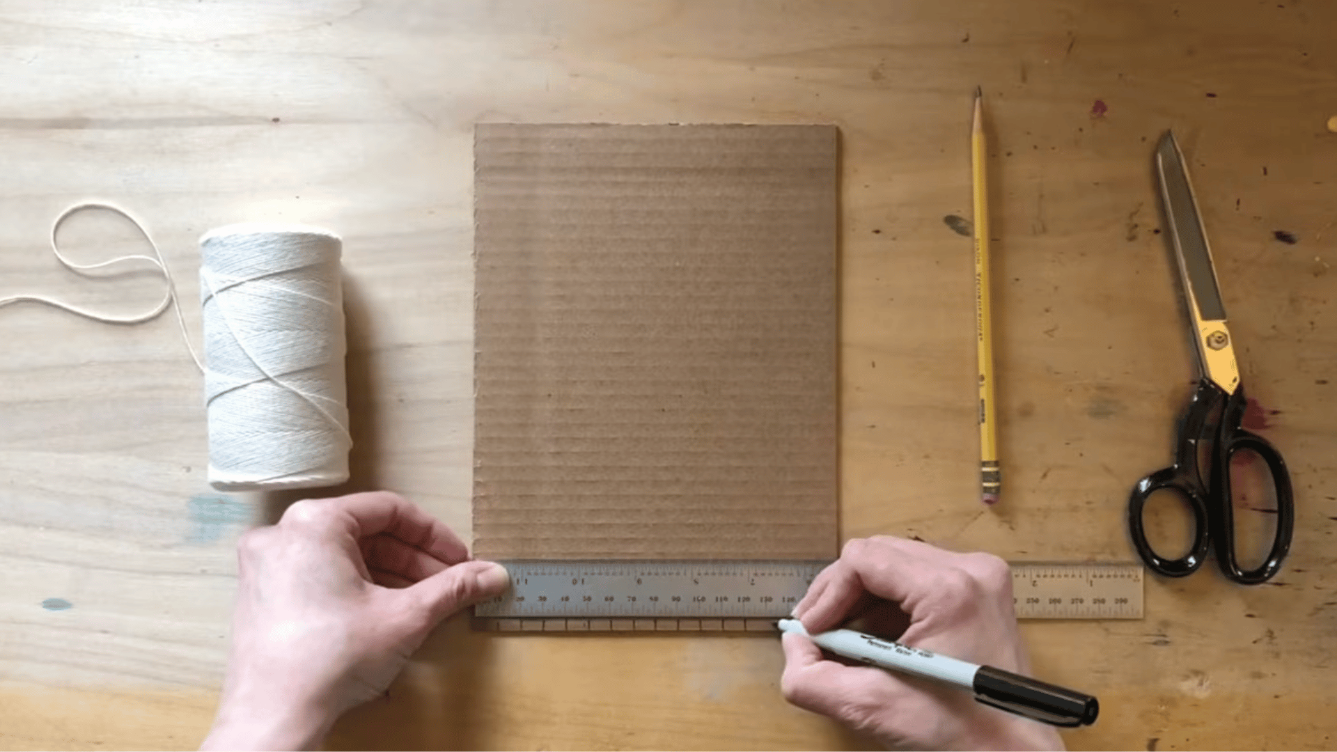 using a ruler and sharpie to mark evenly spaced notches along the top of the cardboard for the loom setup.