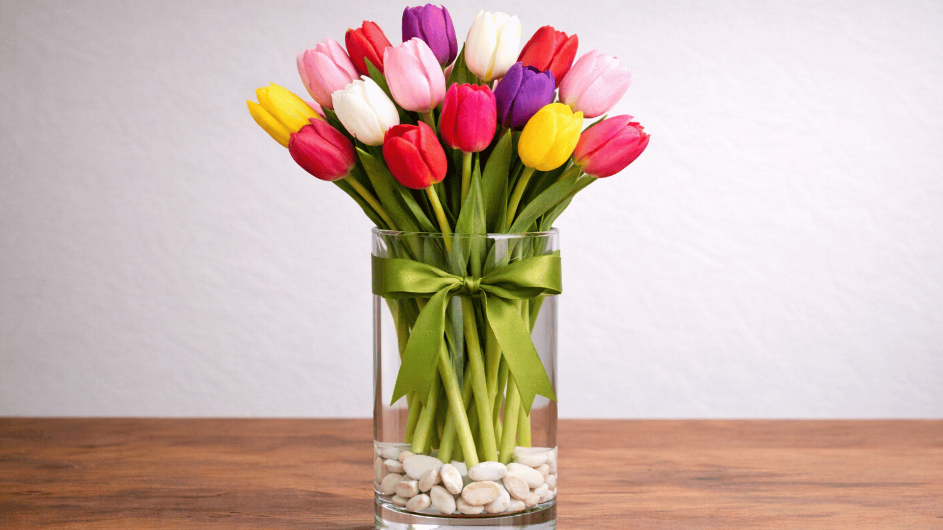 vibrant tulip bouquet arranged in a clear vase with a green ribbon and stones.
