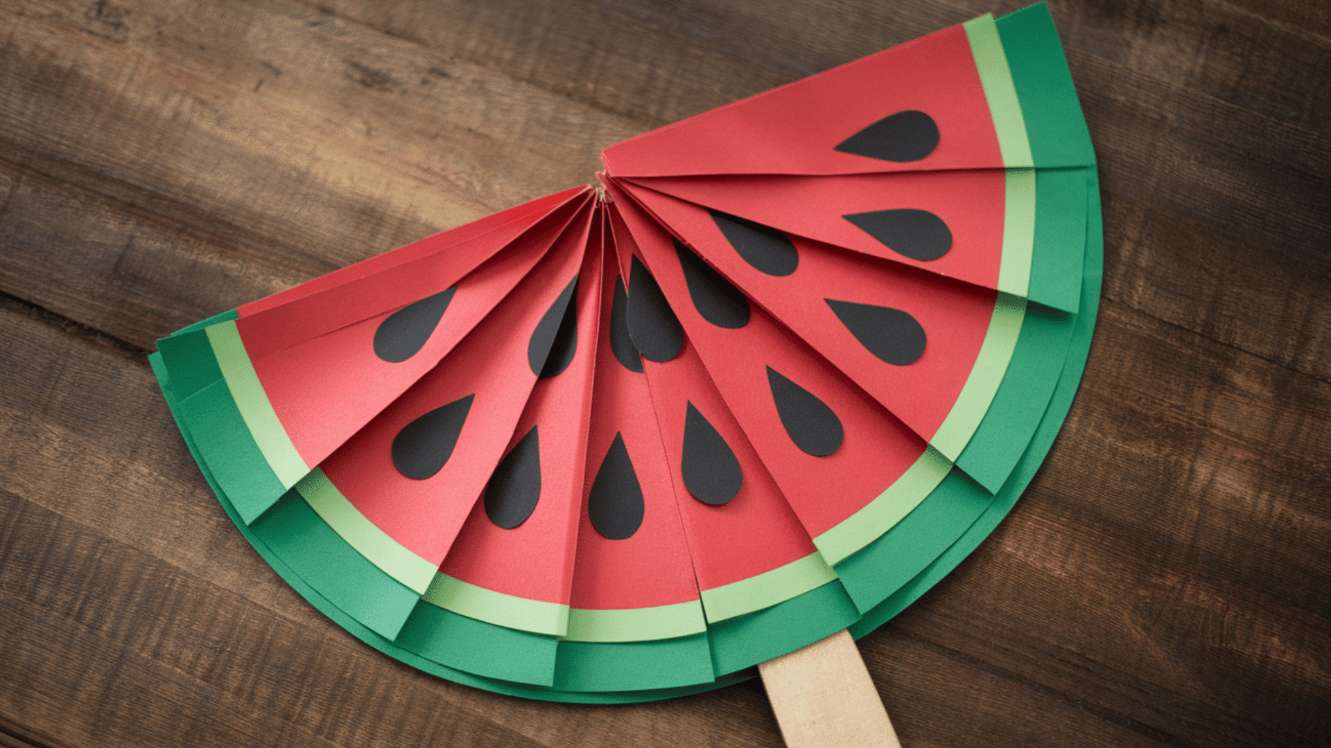 watermelon-shaped fan made from red and green paper with black seed designs and popsicle stick handle (1)