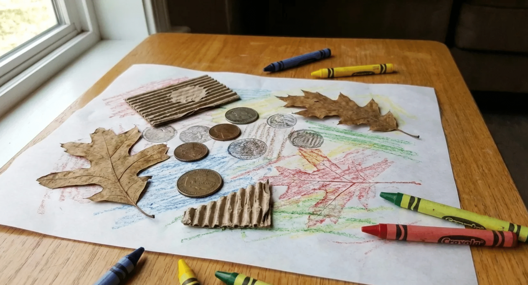 white paper over a textured leaf and rubbing a crayon across the surface to reveal a colorful nature print at home.