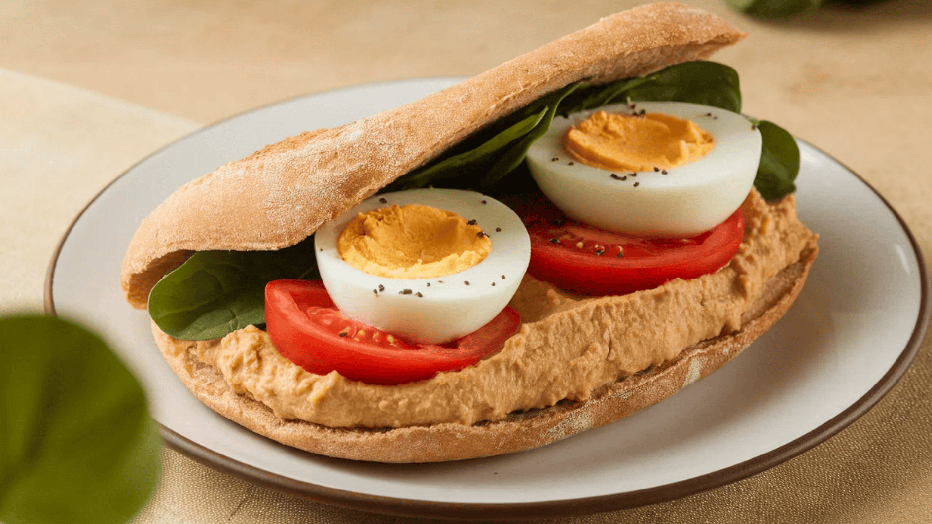 whole-wheat pita filled with hummus, sliced boiled eggs, tomato, and spinach, sprinkled with black pepper