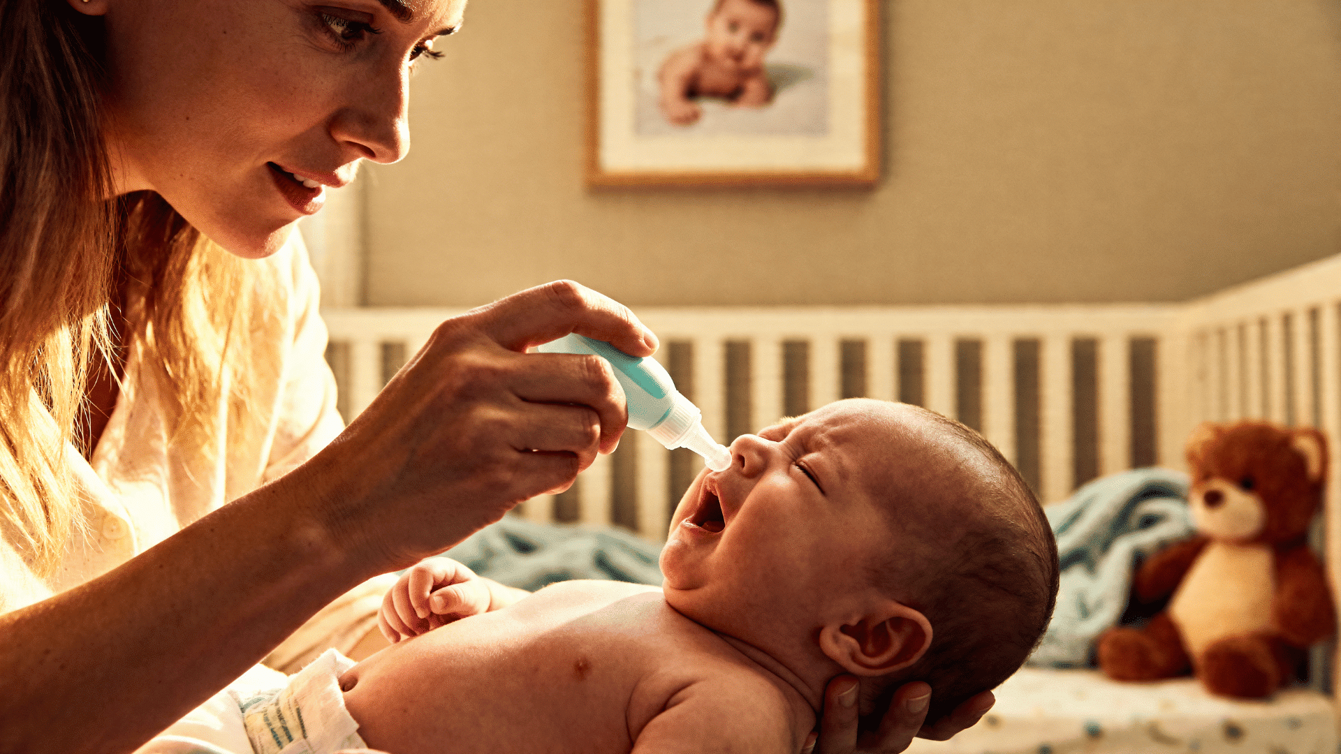 A caring mother carefully applying nasal saline drops to her sneezing newborn baby in a warm nursery room