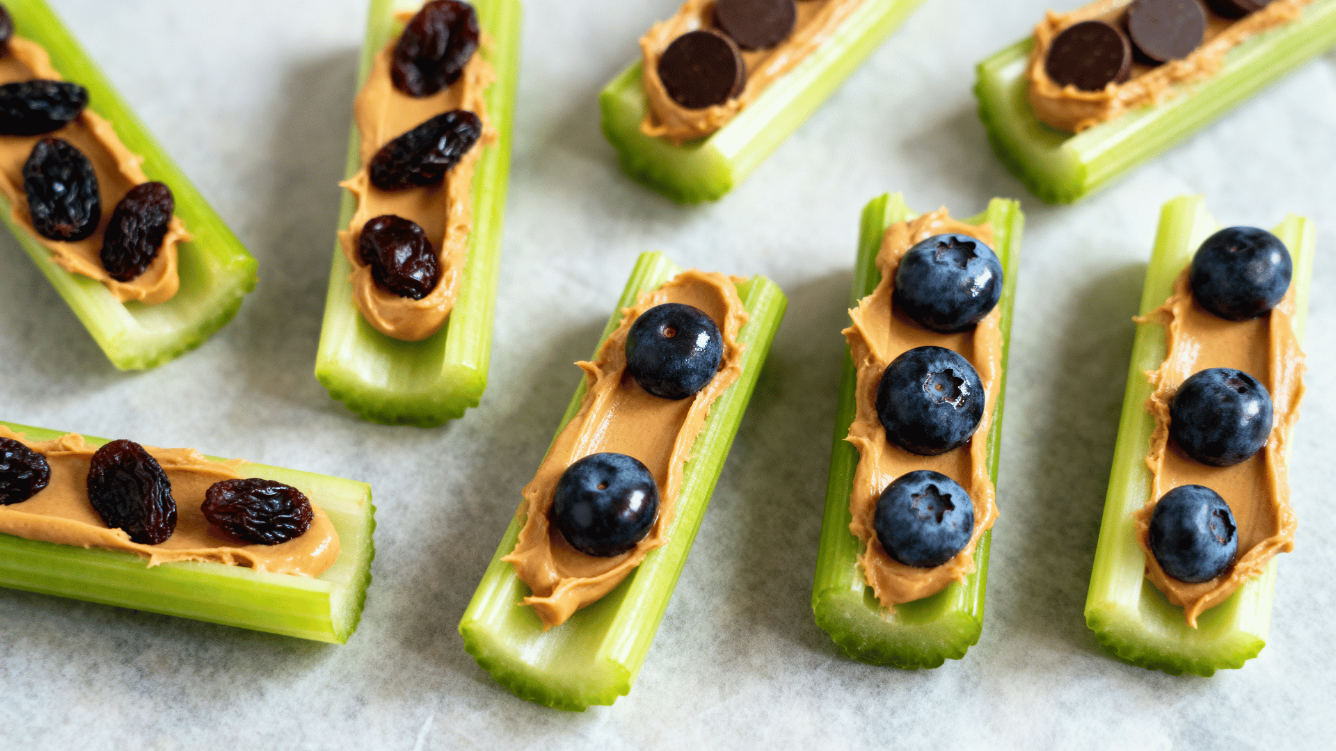 Celery sticks filled with peanut butter and topped with raisins, blueberries, and chocolate chips on a tray