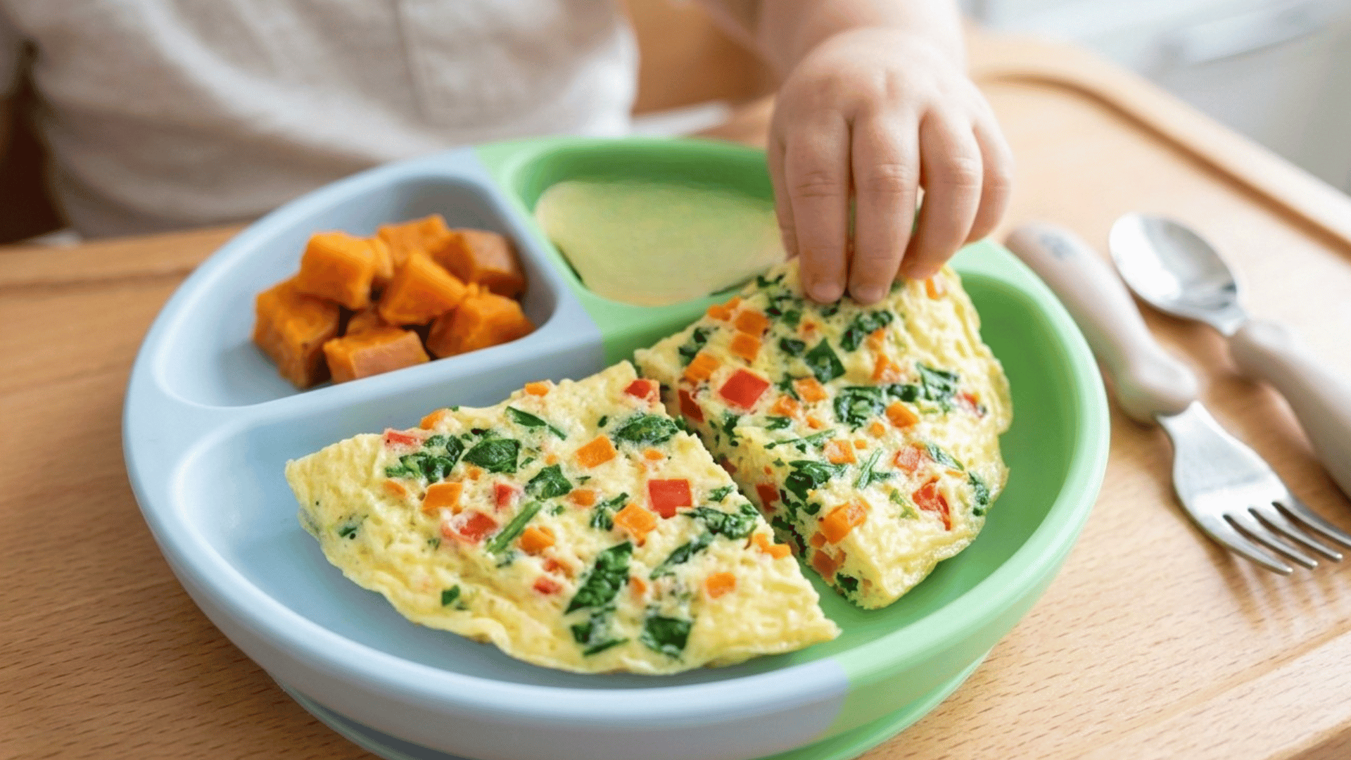 baby hand reaching for veggie omelette with sweet potato and banana slices.